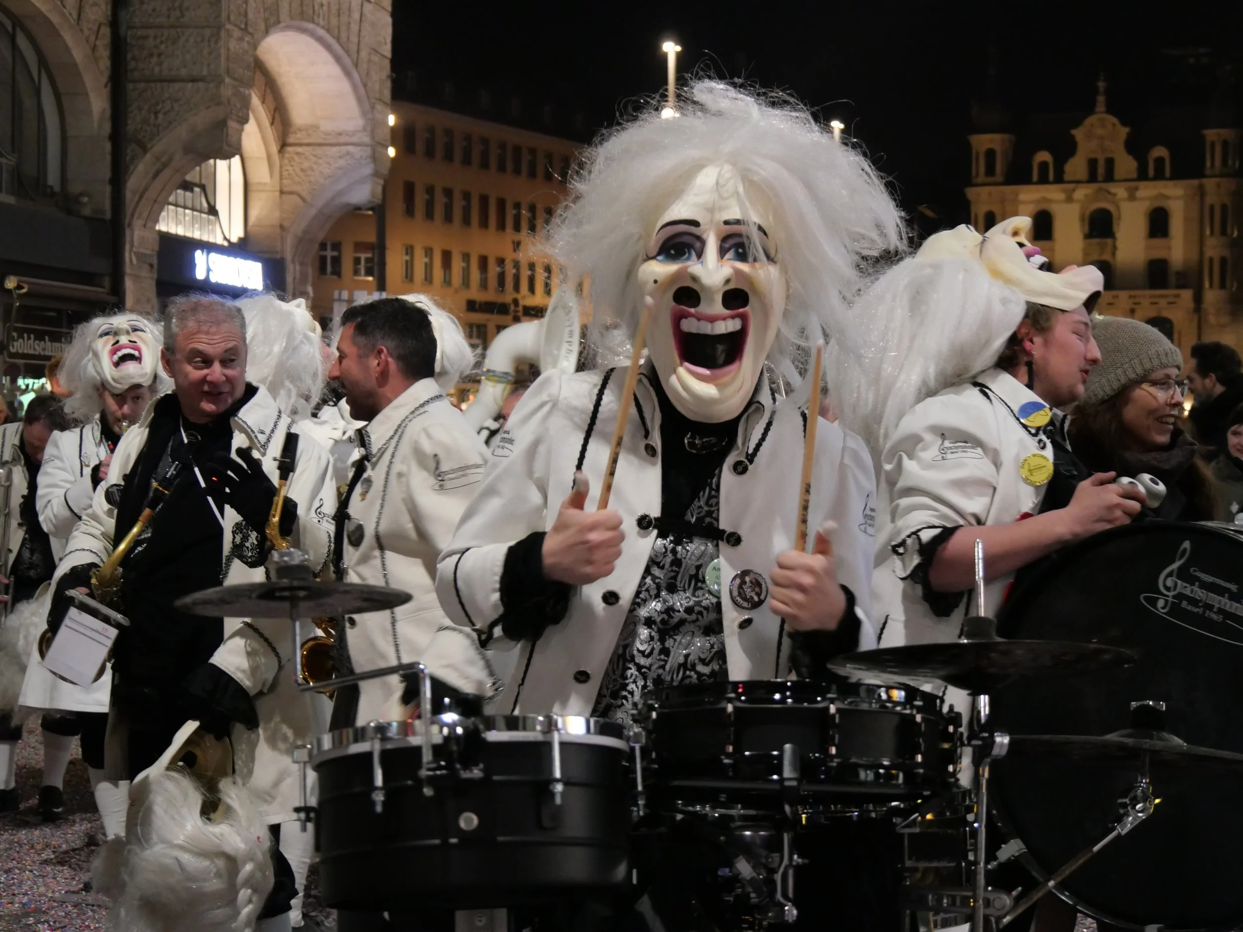 Menschen in Kostümen mit Masken, die auf einer Straßenparade mit Musikinstrumenten feiern, nachts, in einer Stadt