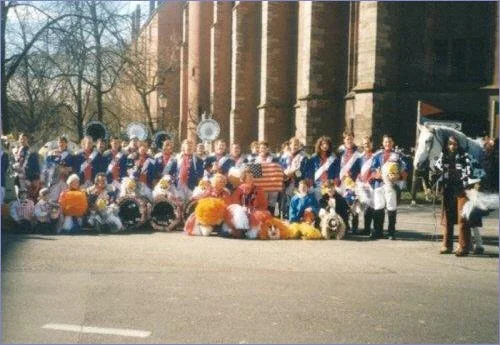 Eine Gruppe von Menschen, die an einem festlichen Anlass teilnehmen, mit einigen in Kostümen, vor einem historischen Gebäude im Freien.