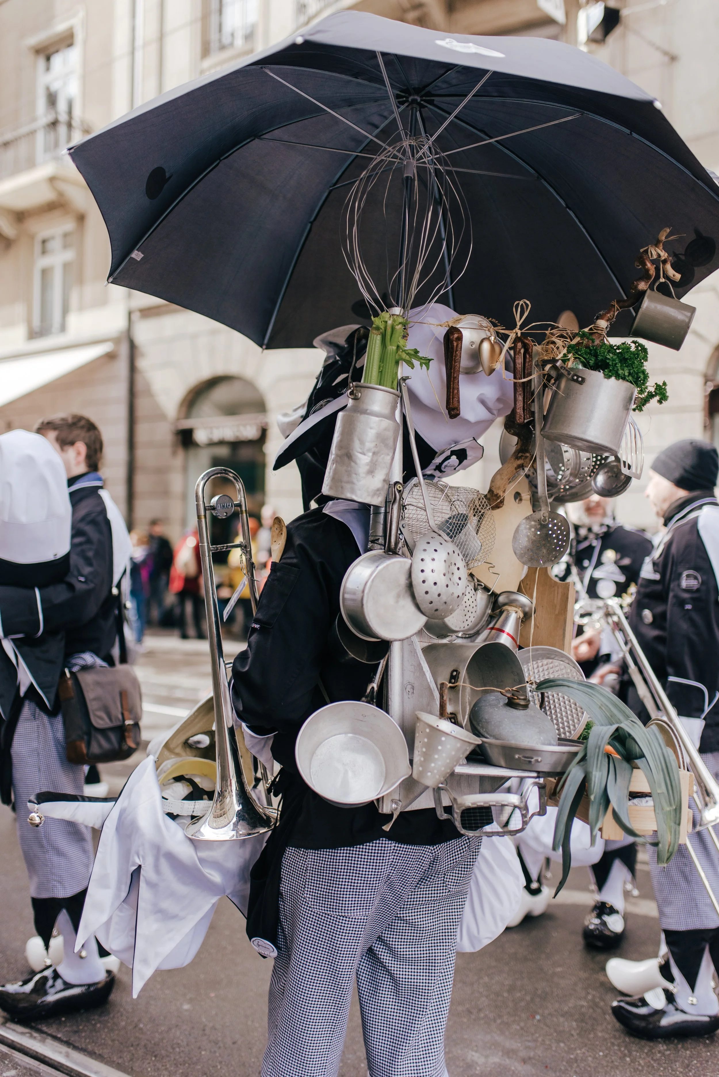 Person trägt eine Tragetasche voller Küchenutensilien, die an einem Regenschirm befestigt sind, bei einer Straßenveranstaltung.
