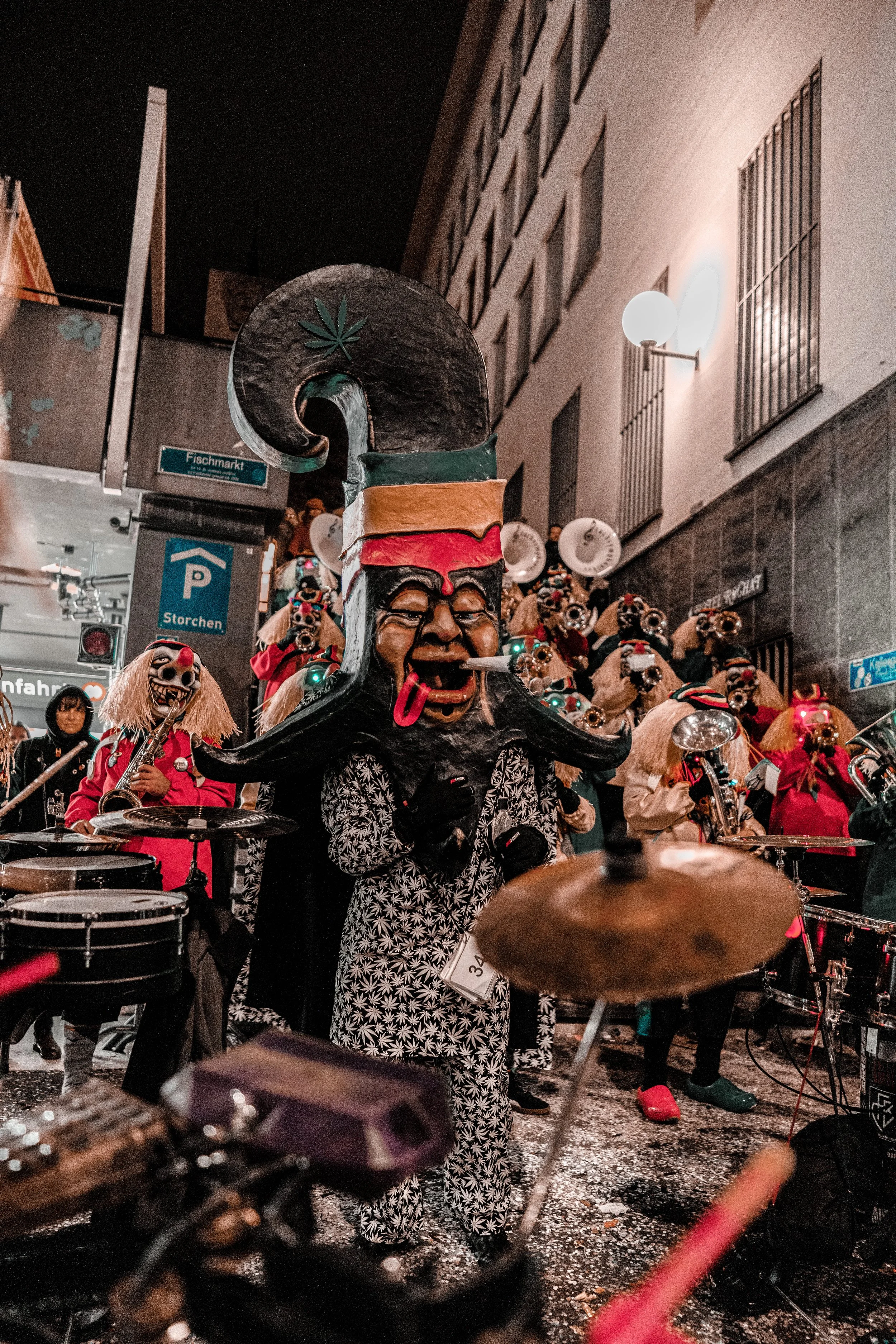 Menschen in Kostümen und Masken bei einem Straßenfest mit Musik und Instrumenten in der Nacht.