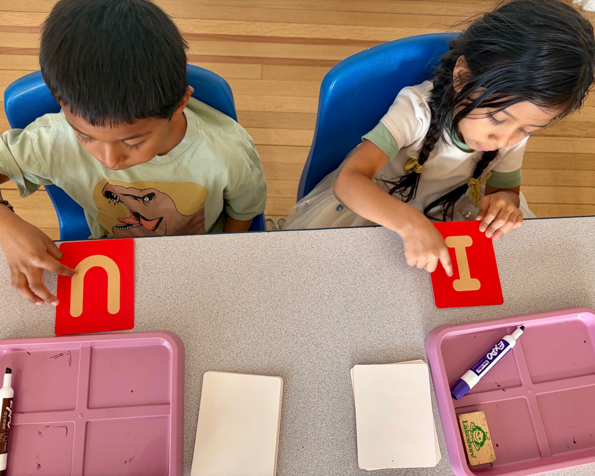 Children sitting at a table playing with cards that have the letter 'O' on them. Children partaking in a learn to read exercise during a literacy tutoring session.