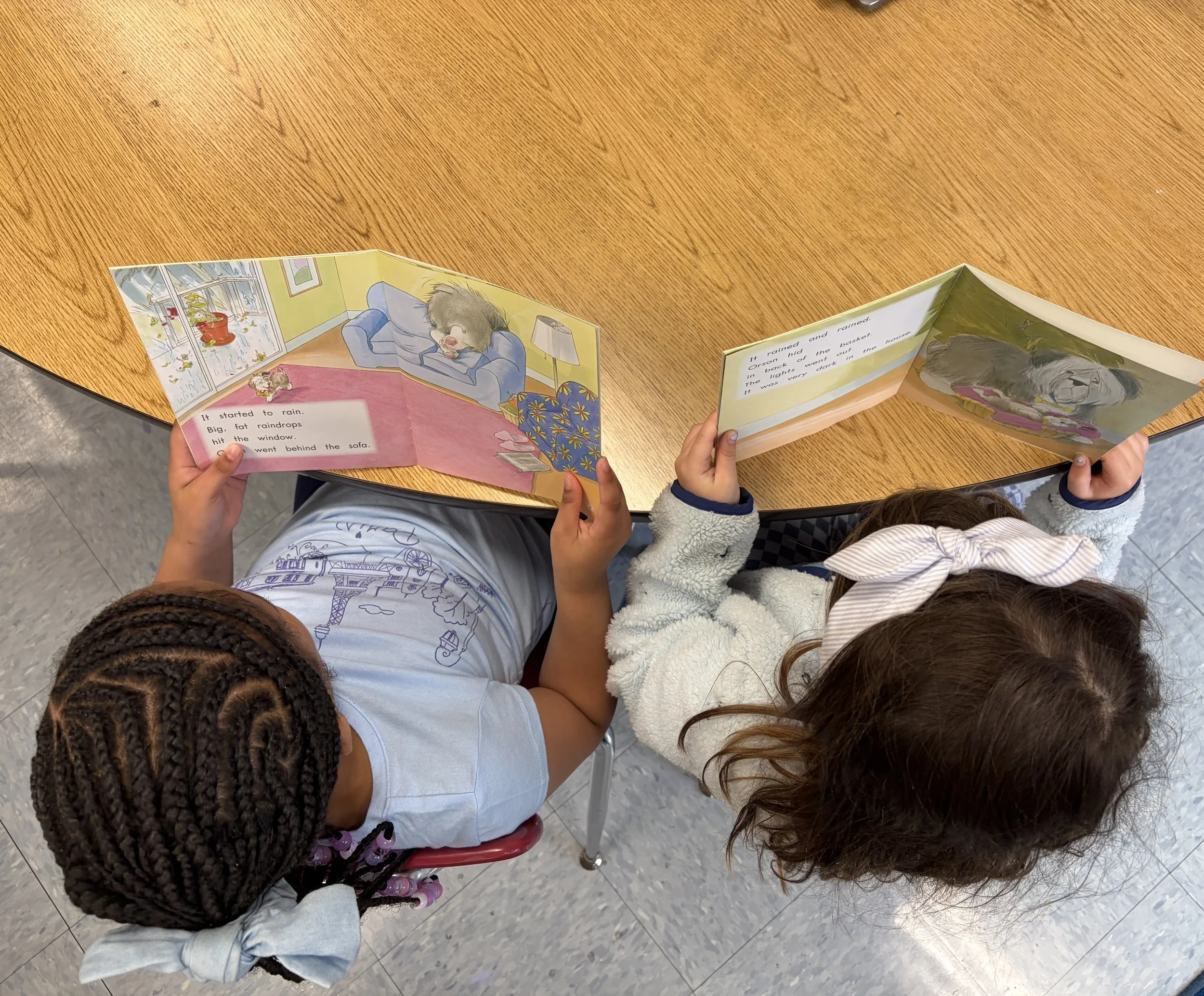 Children sitting at a table learning to read a children's book at a literacy tutoring session.