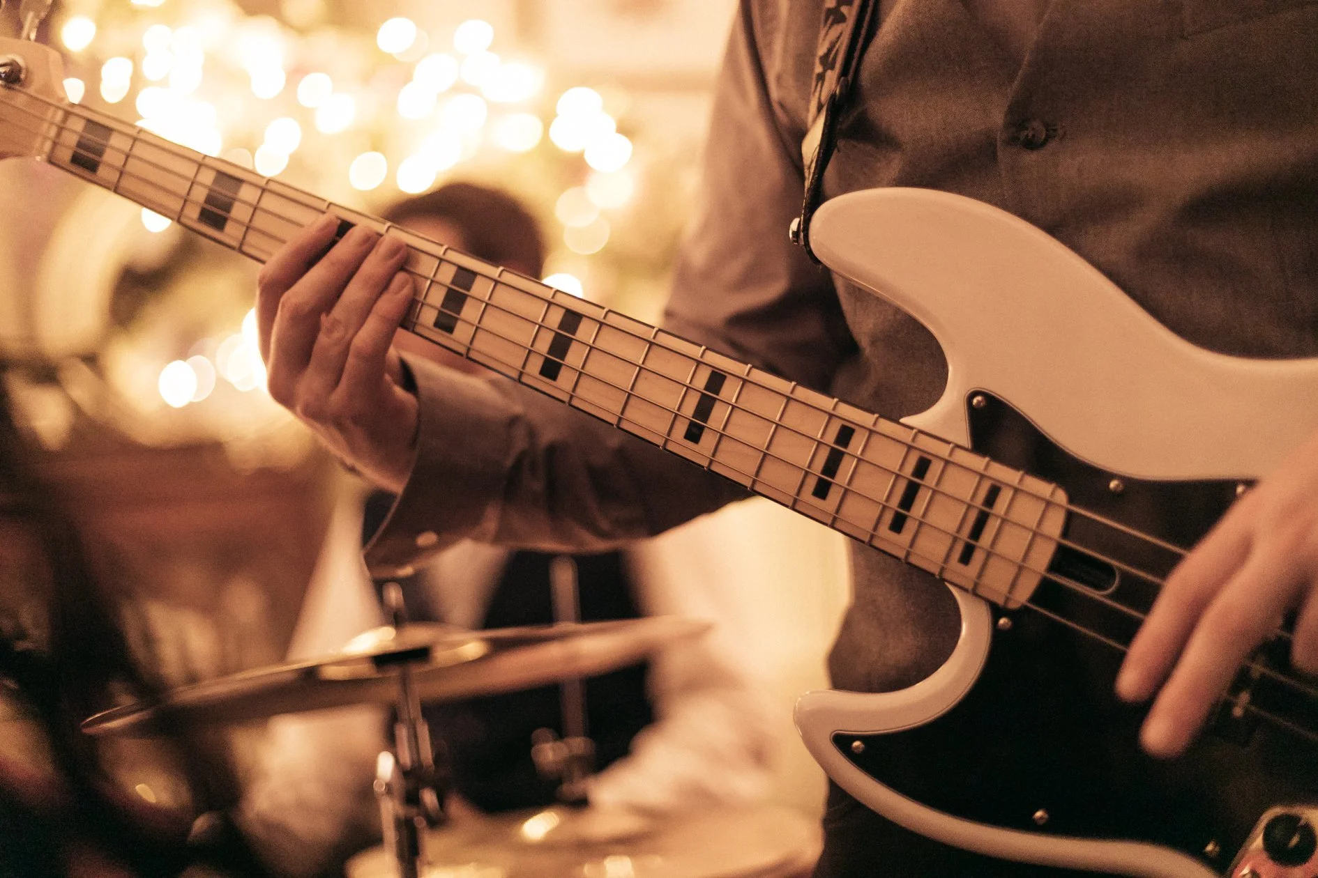 Person playing an electric guitar during a live music performance, with blurred warm lights in the background.