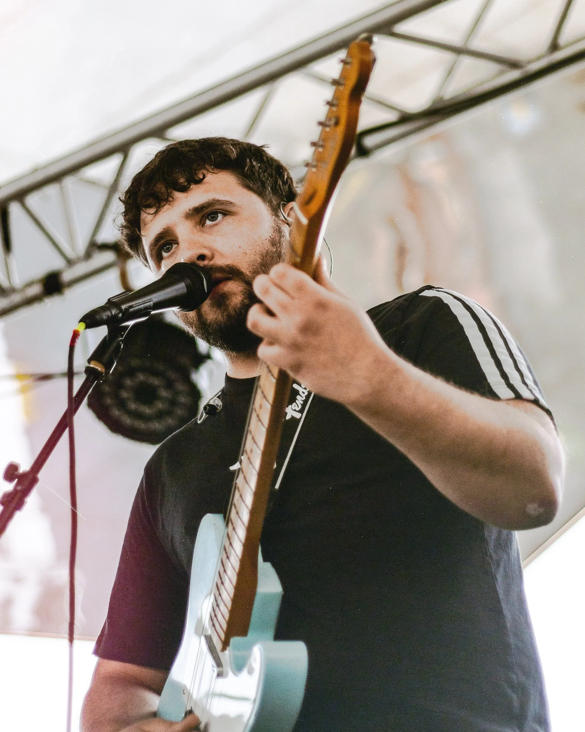 A young man with a beard and curly hair singing into a microphone while playing an electric guitar.