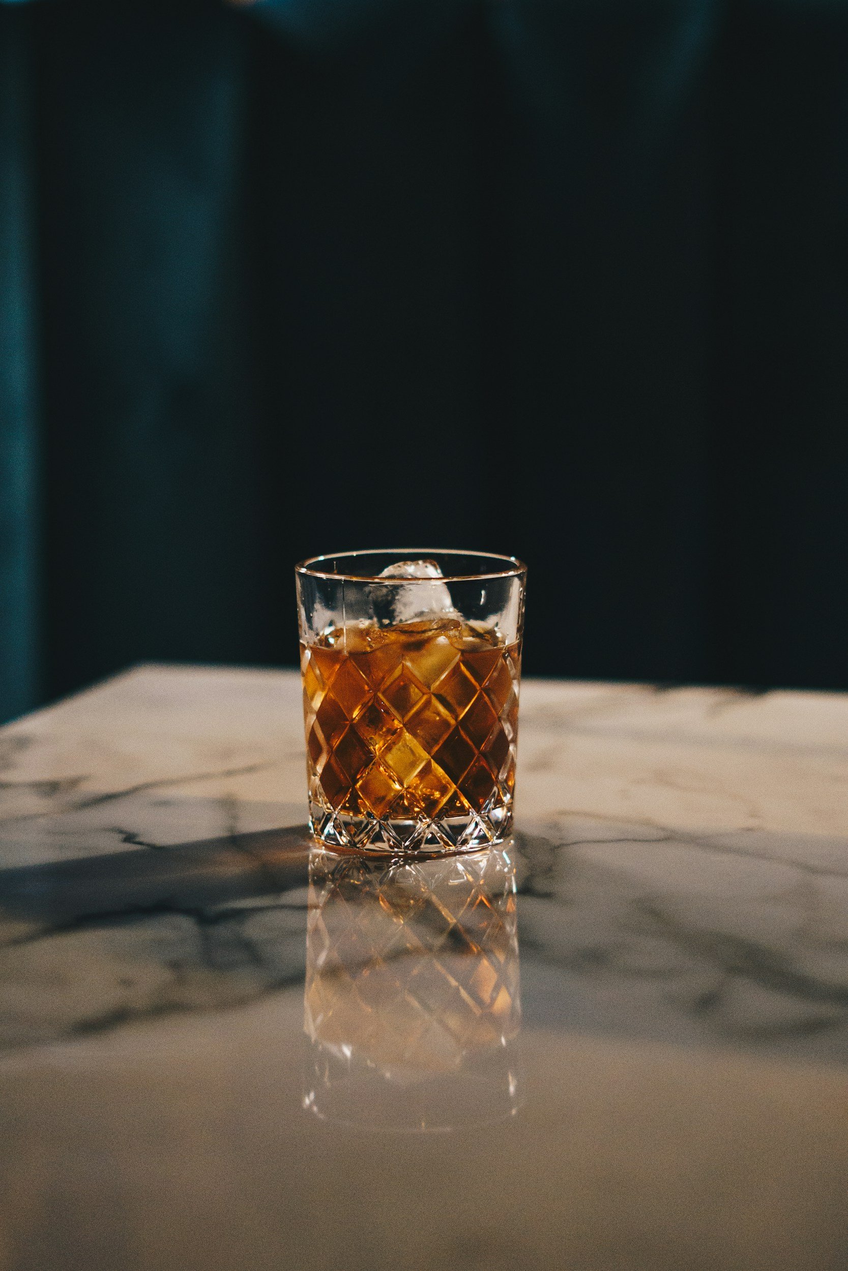 A glass of whiskey with ice cubes on a marble table.