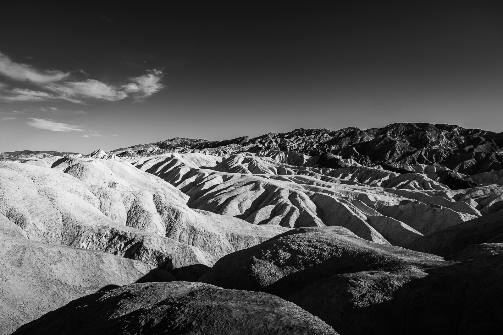 Black and white photo of a rugged mountainous desert landscape with layered ridges and valleys.