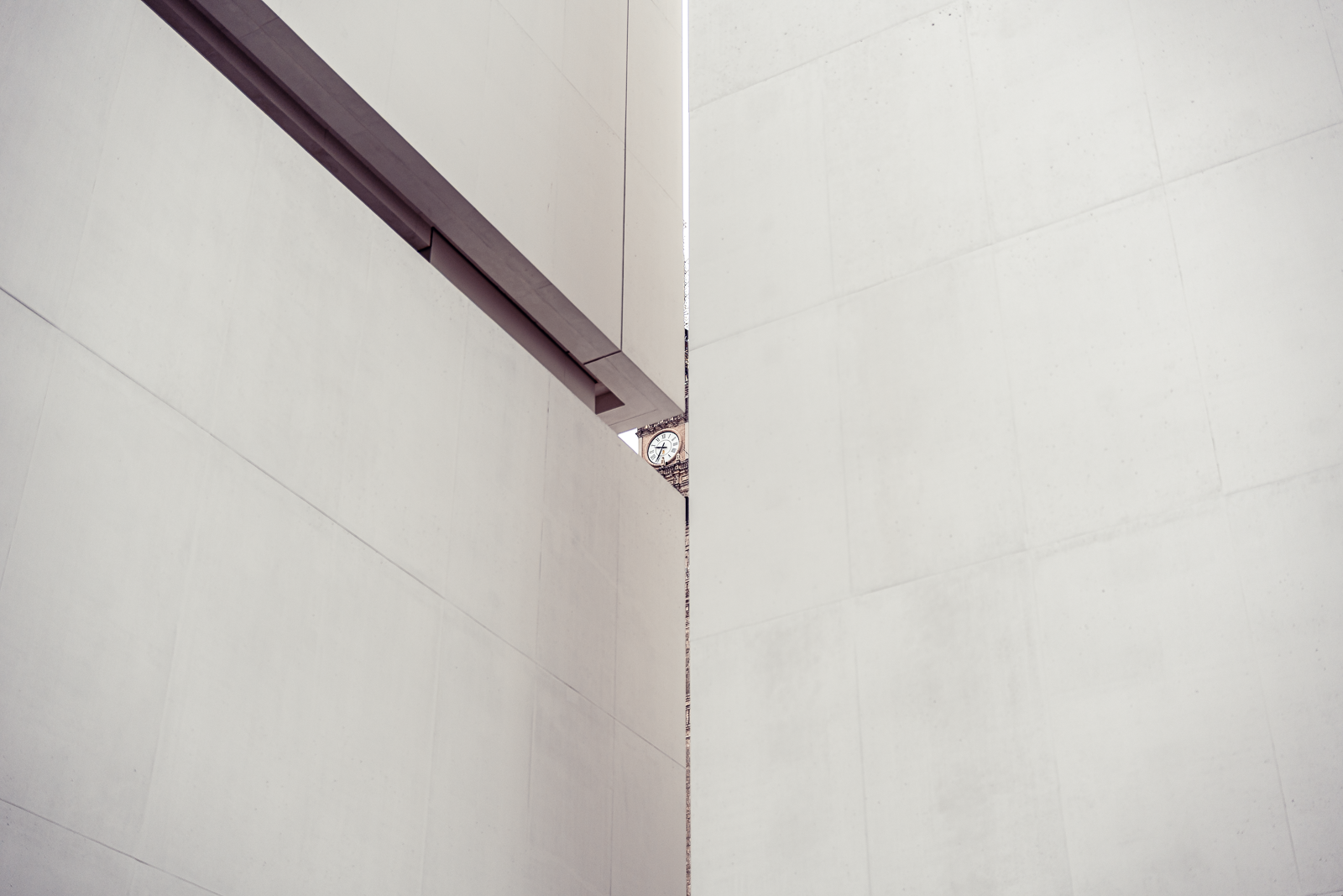 A narrow space between two large beige concrete walls with a small clock visible in the distance.