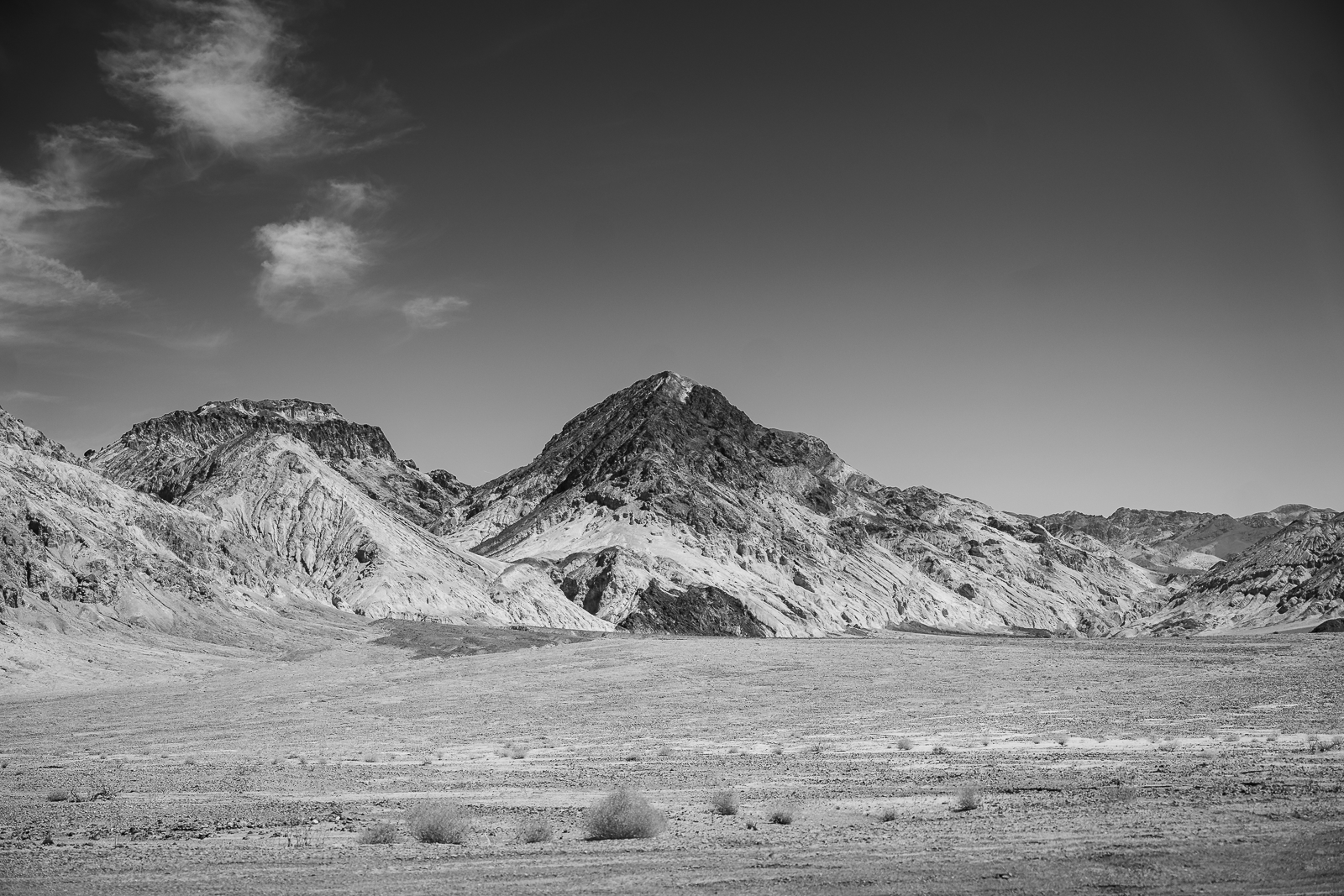 Black and white photo of a mountainous landscape with a wide, flat foreground and sparse vegetation.