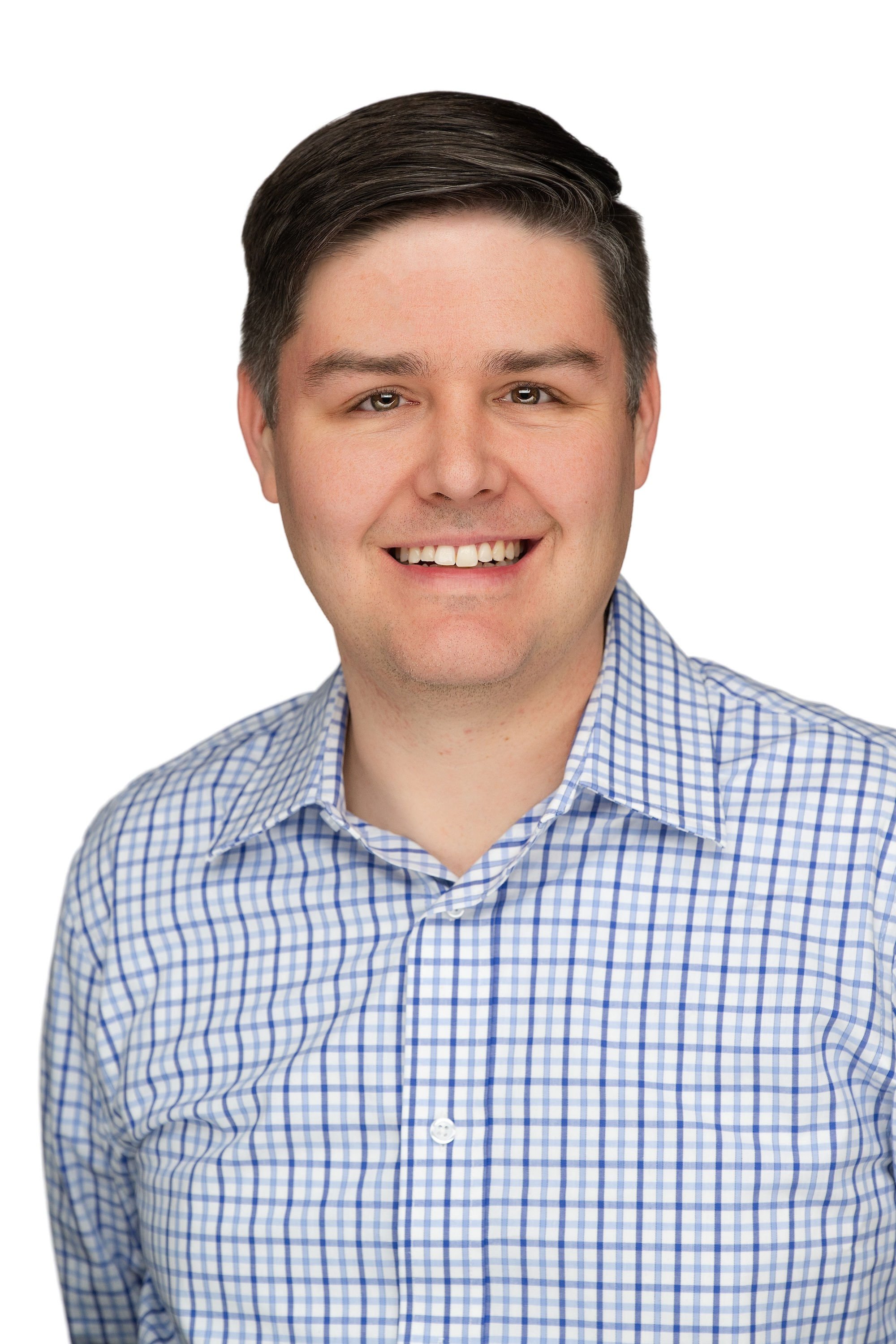 A young man with dark hair smiling, wearing a blue and white checkered shirt, against a plain white background.