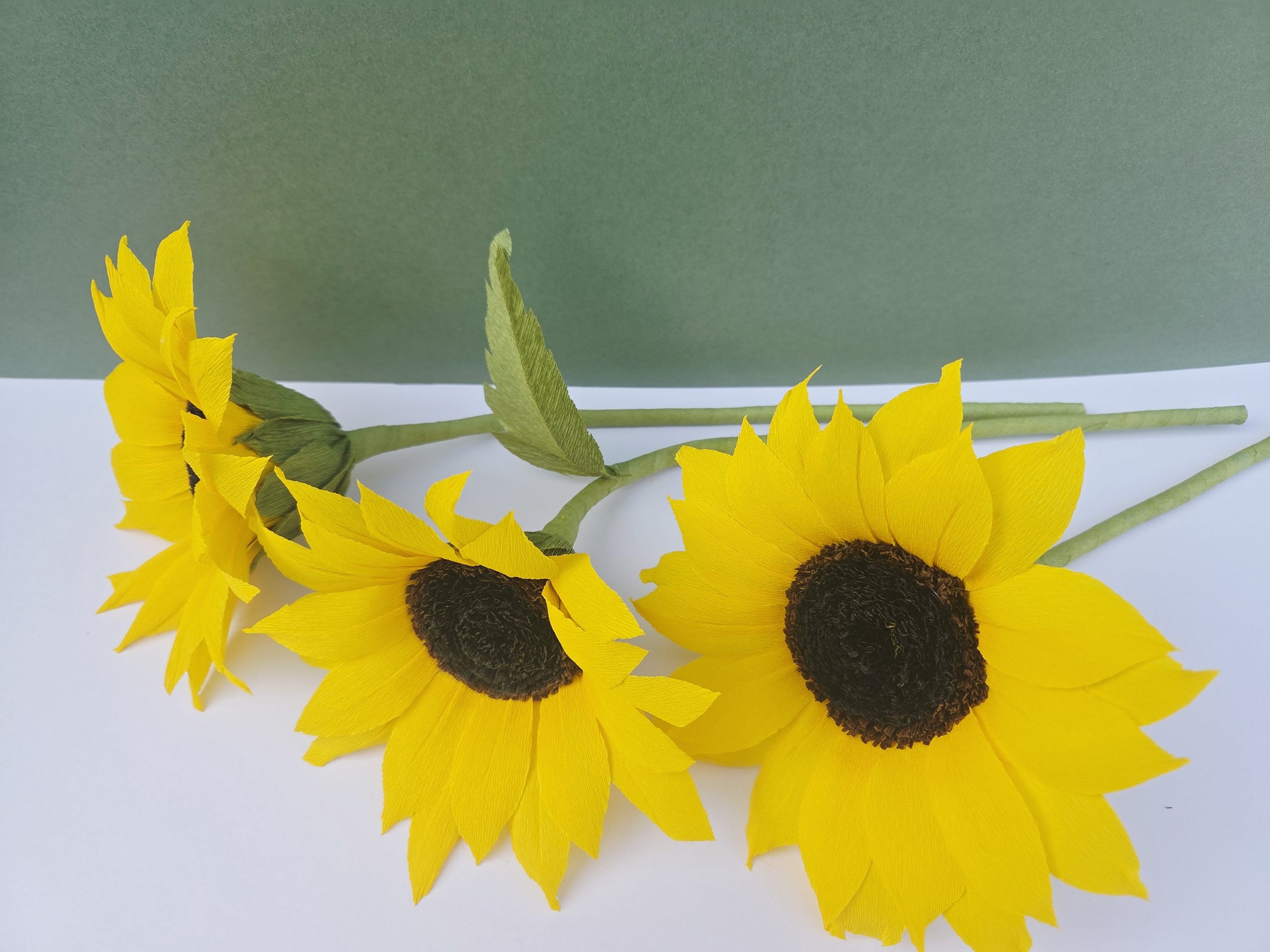 Three artificial sunflowers with yellow petals and dark centers lying on a surface with a green background.