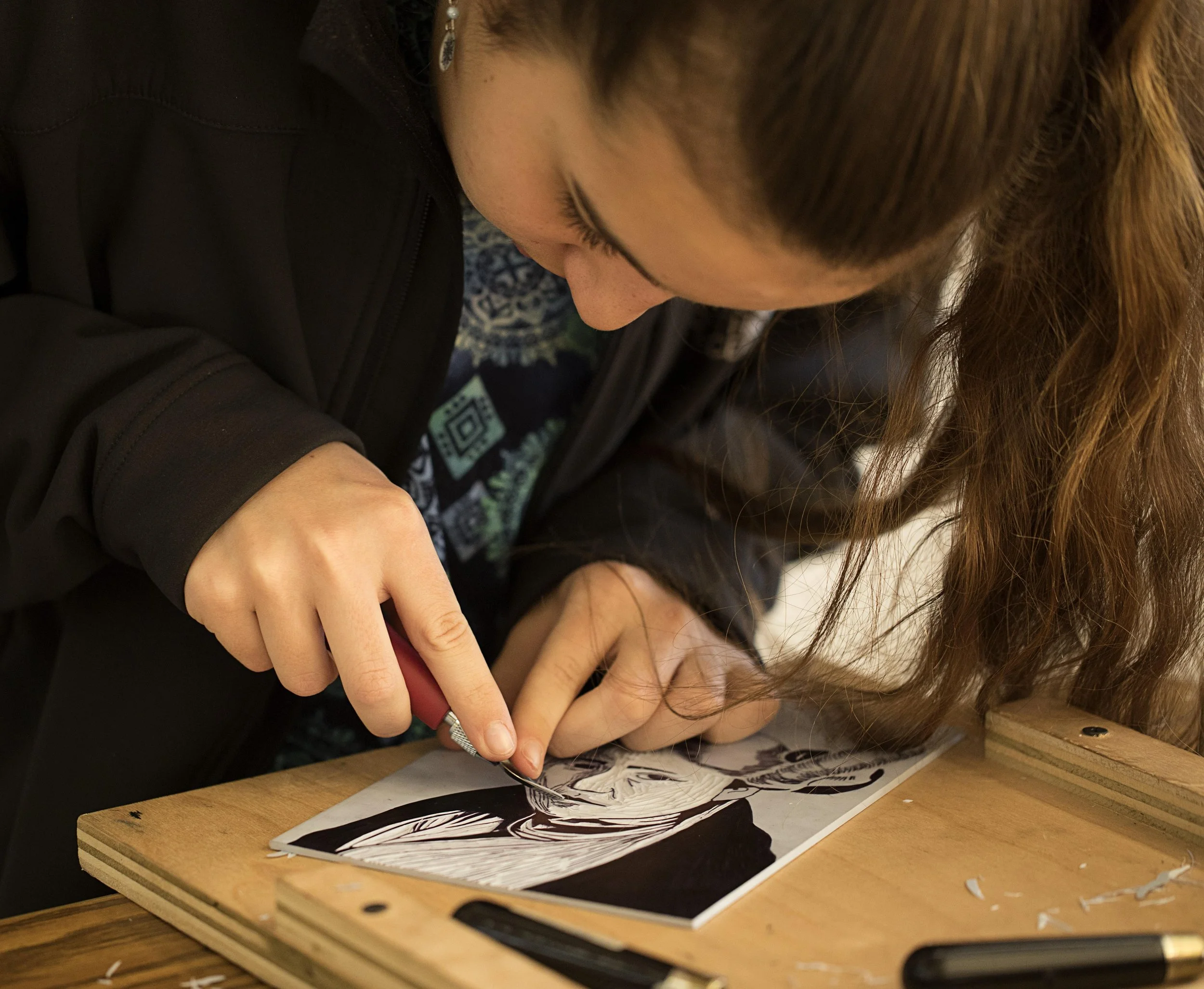 A middle school girl at Rudolf Steiner School of Ann Arbor is intently focused on her art project, which is a linocut of a woman.