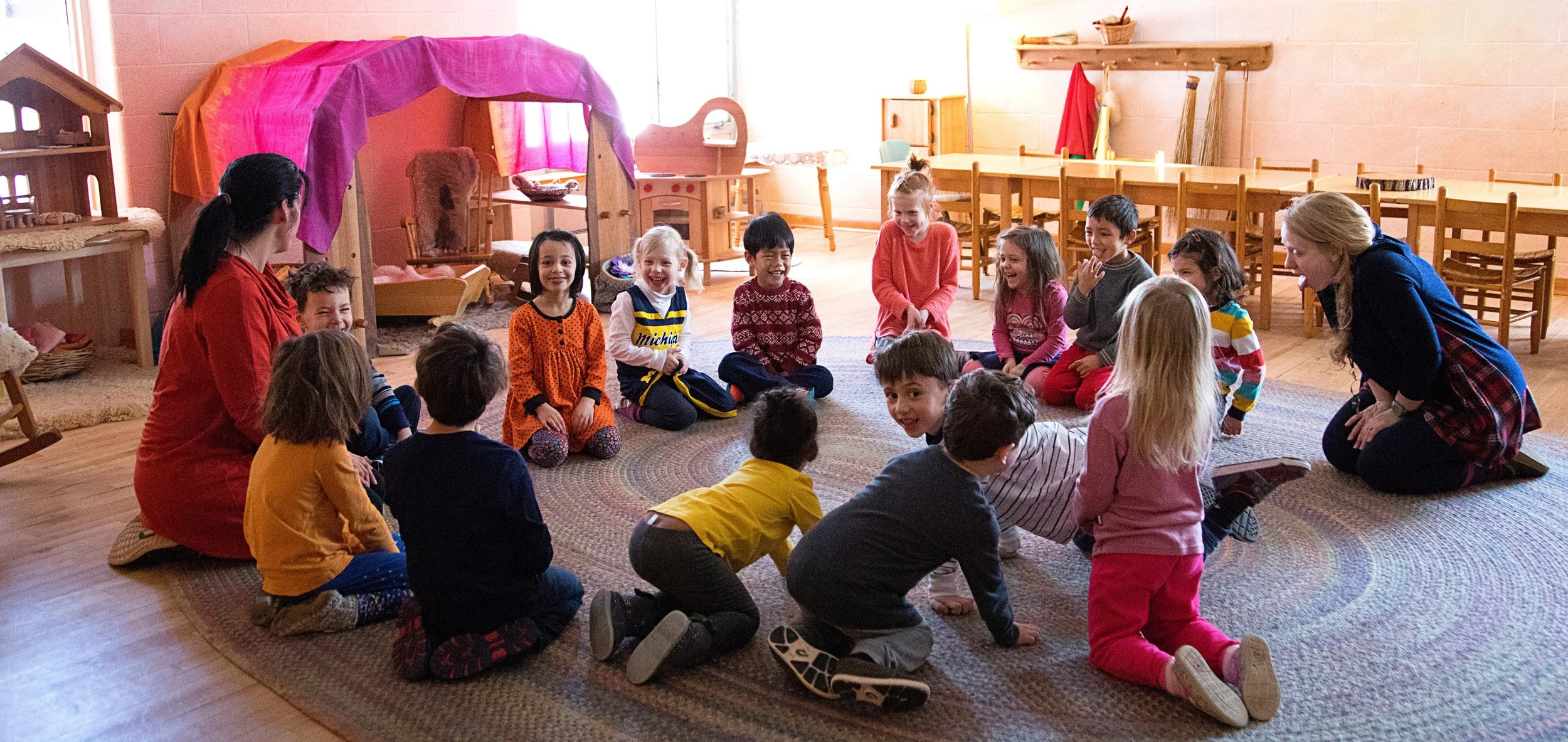 A group of kindergarteners at Rudolf Steiner School of Ann Arbor are playing on the floor of the classroom, laughing together.