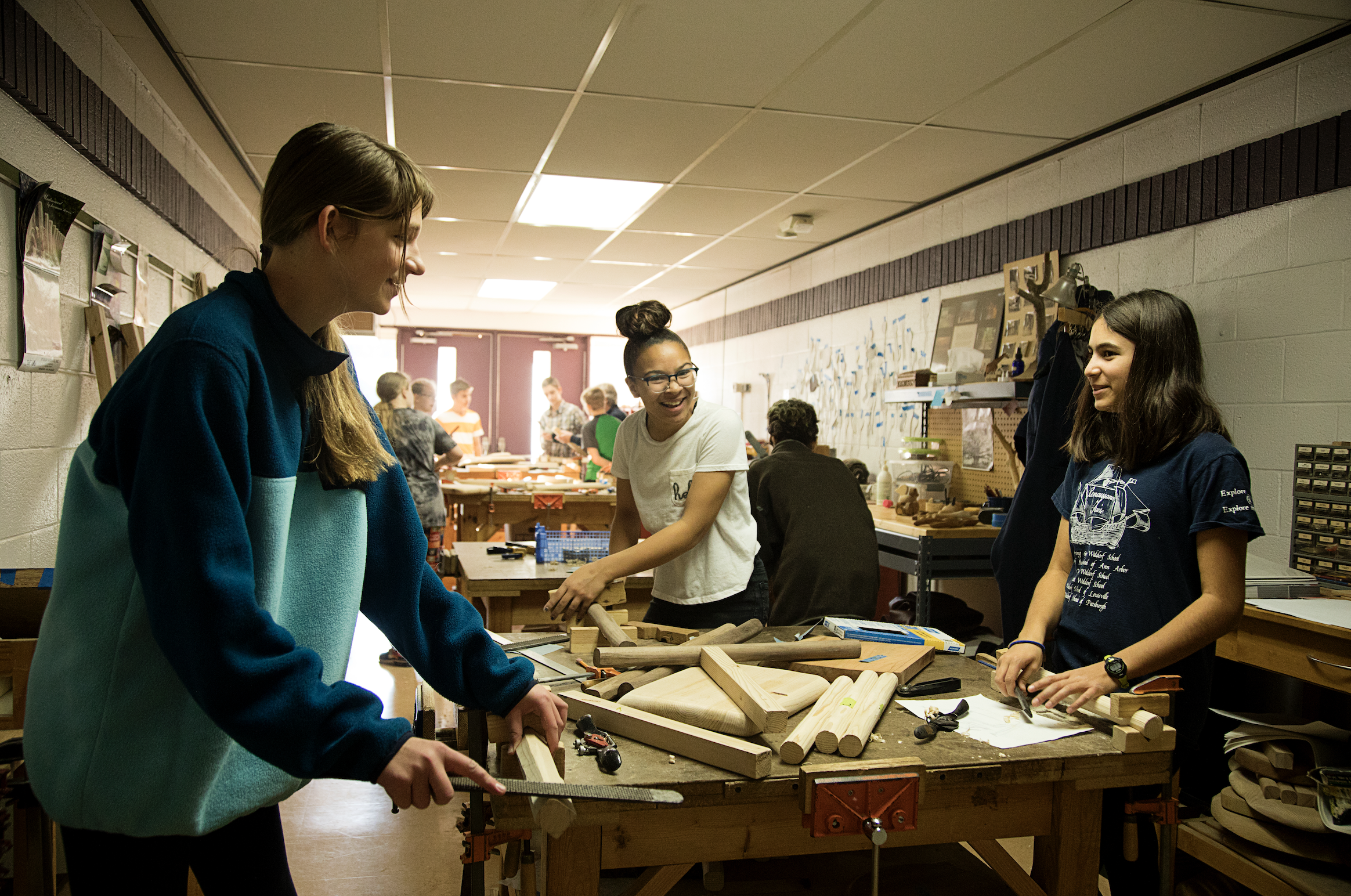 A group of middle school students at Rudolf Steiner School of Ann Arbor are pictured working on their woodworking project together in the studio, smiling and laughing together.