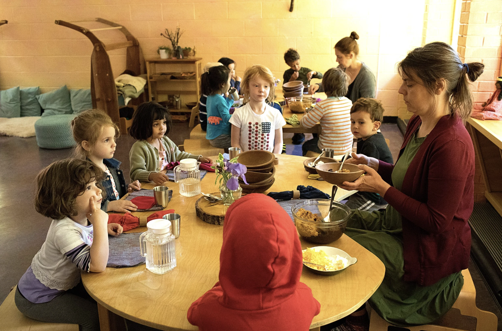 A group of kindergarteners at the Rudolf Steiner School of Ann Arbor are sitting around the table eating out of wooden bowls.