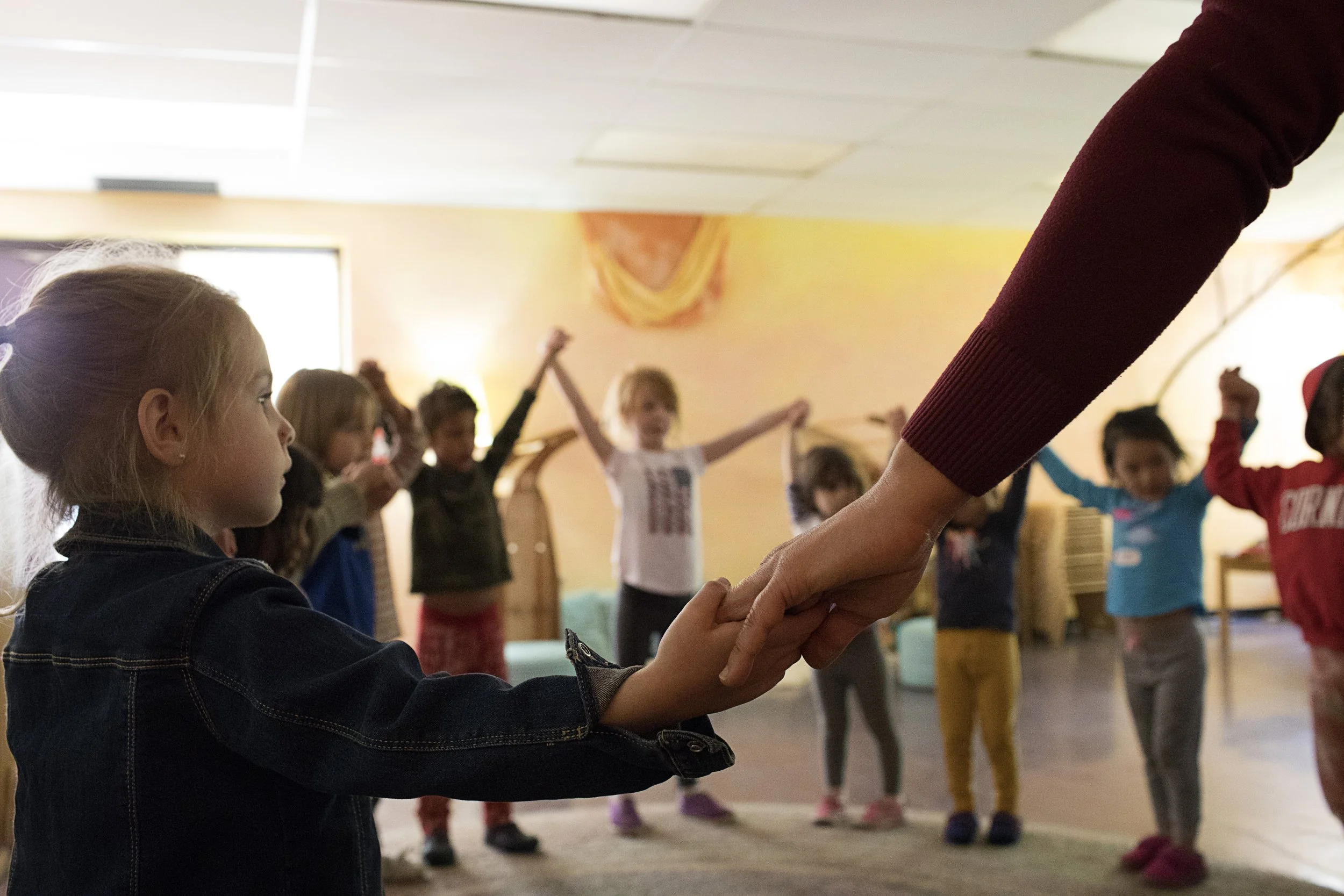 A group of kindergarteners at Rudolf Steiner School of Ann Arbor or holding hands in a circle and some kids are raising their hands into the air together.