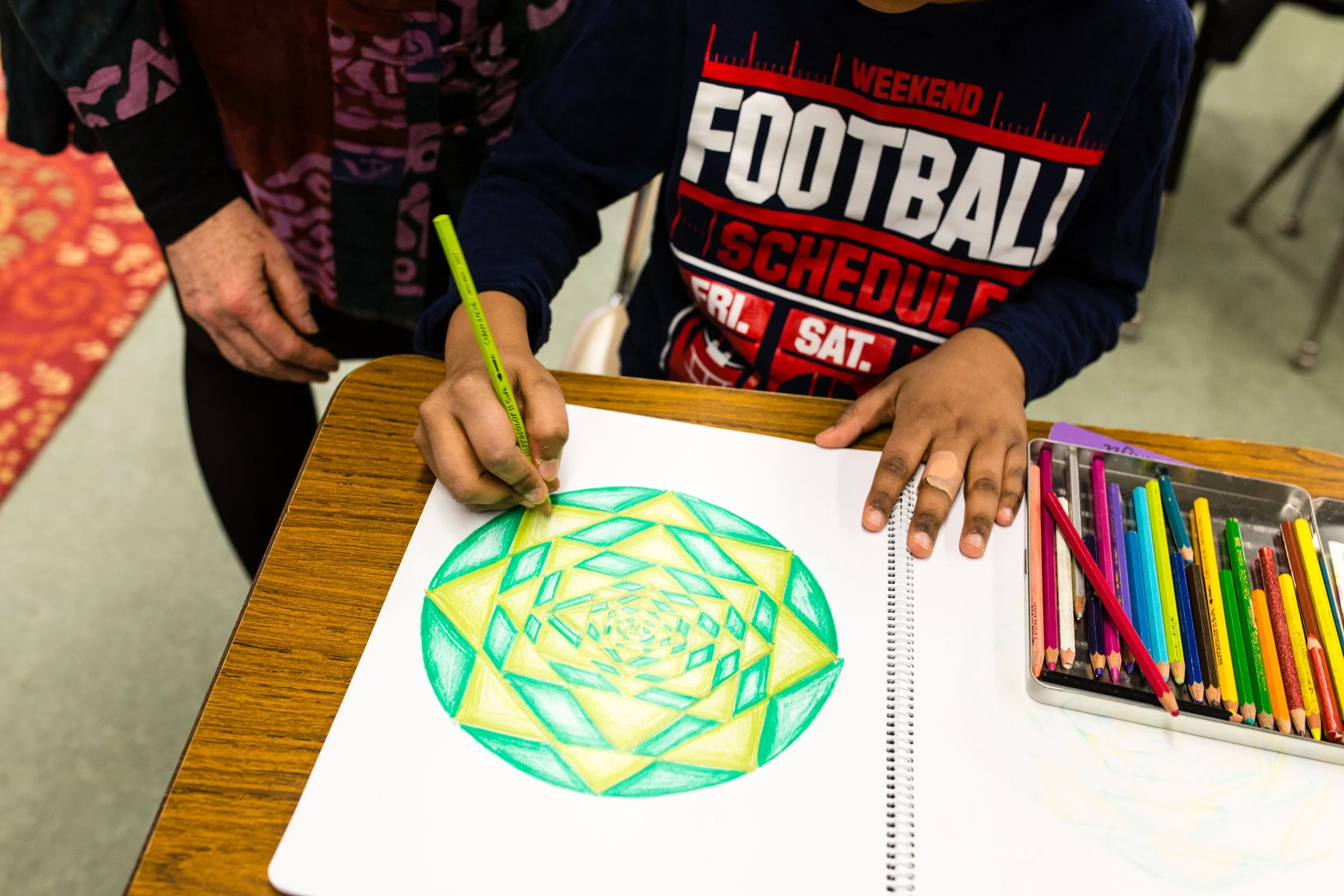 A close of picture of an elementary school student works on his geometry drawing with yellow and green pencils.
