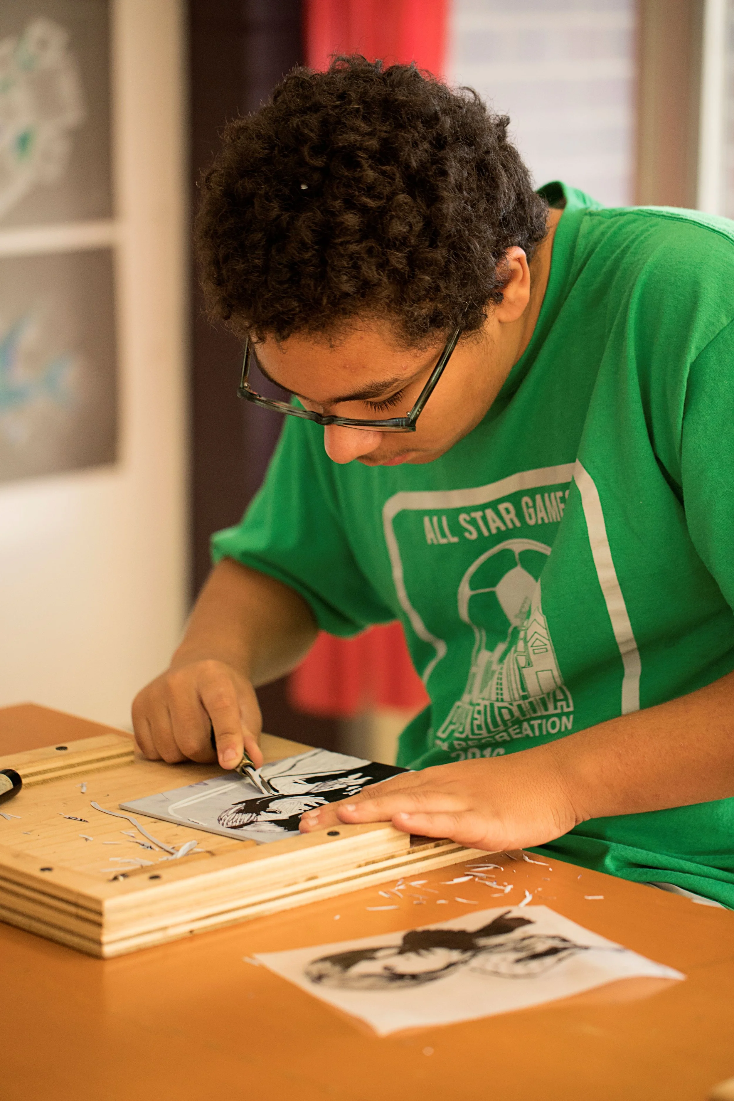 A middle school boy in a green shirt and glasses at Rudolf Steiner School of Ann Arbor is working on a linocut of a woman.