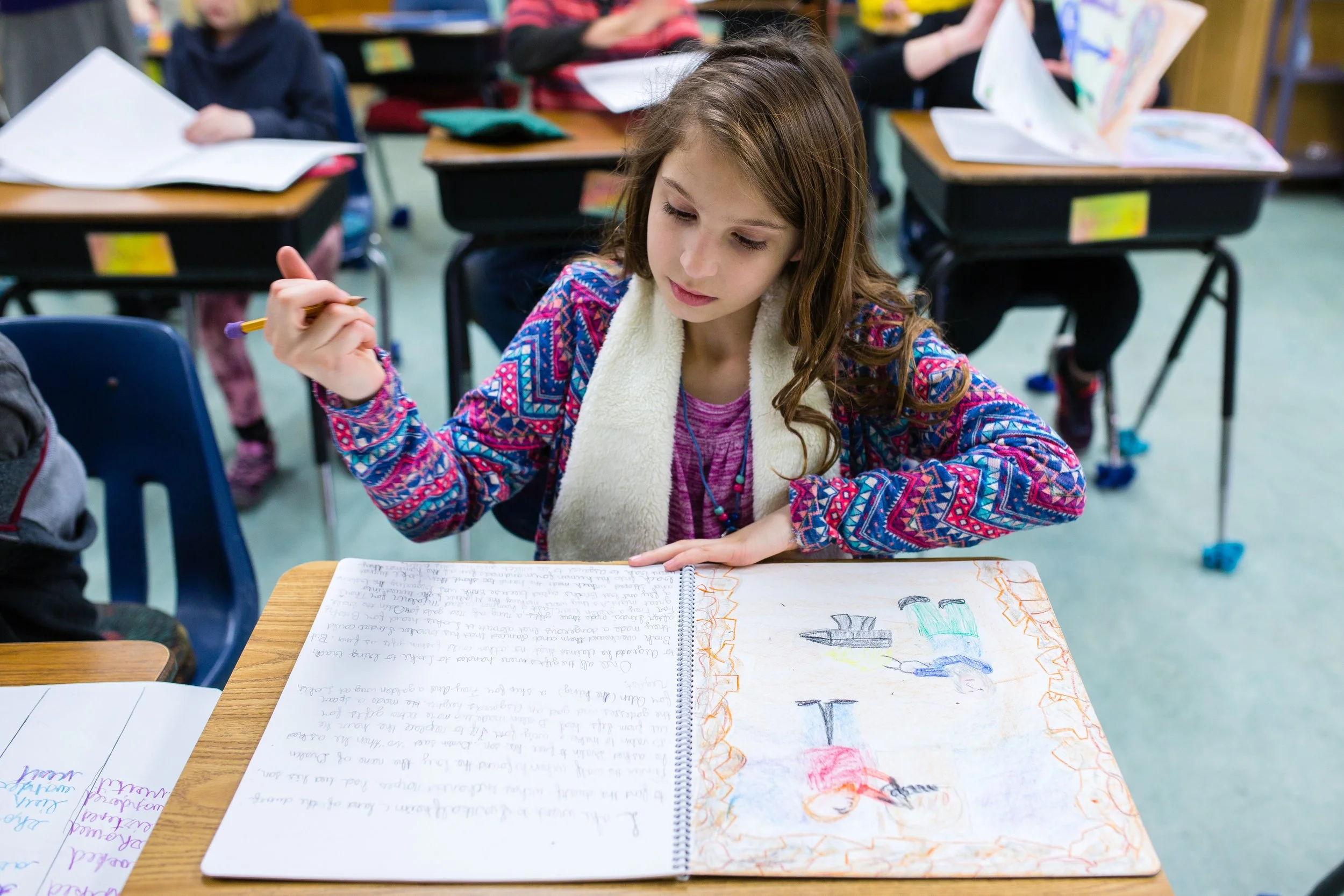 An image of a girl in elementary school at Rudolf Steiner School of Ann Arbor, focused on writing in her handmade main lesson textbook.