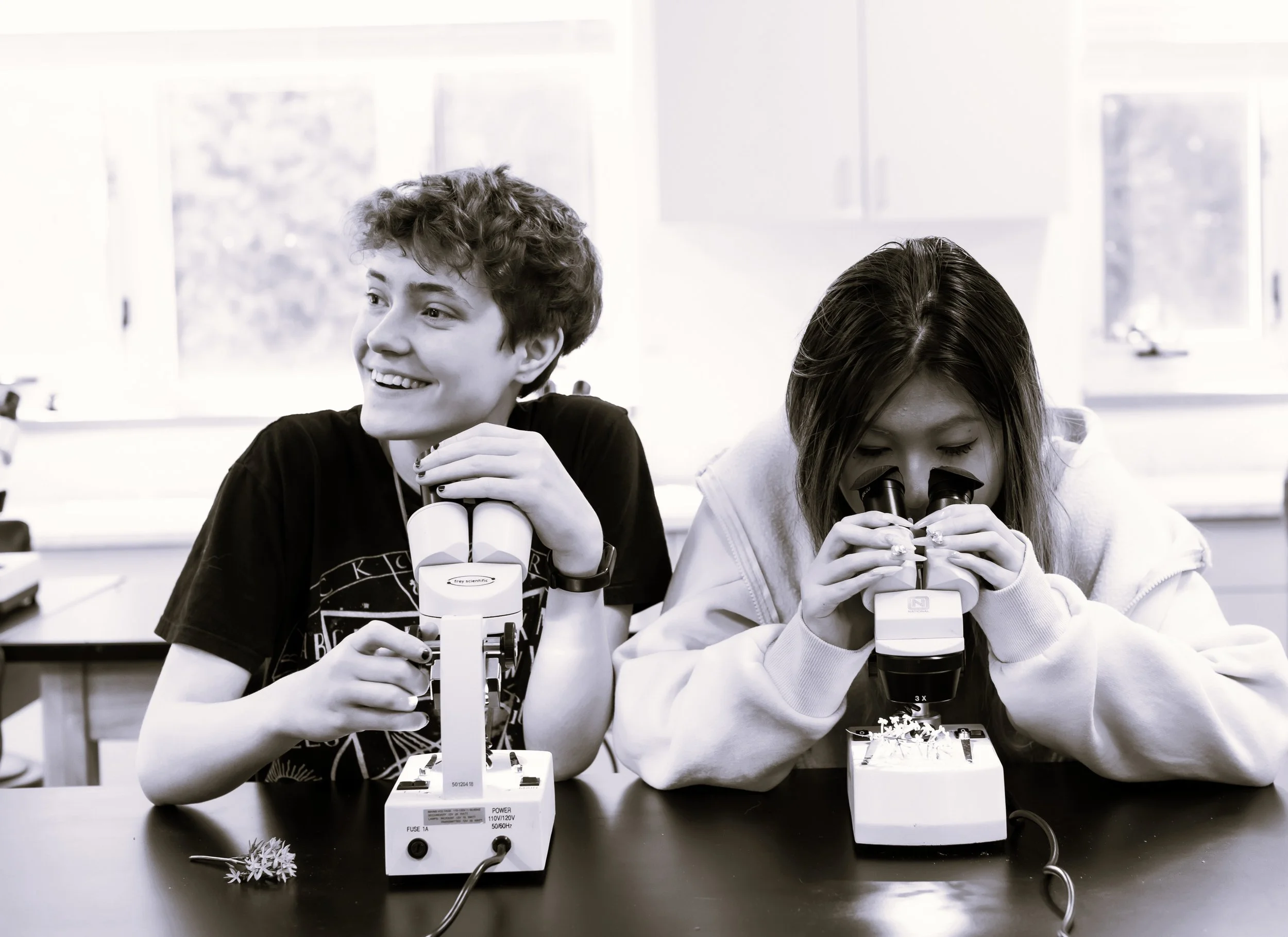A black and white image of a boy at Rudolf Steiner School of Ann Arbor. The boy is smiling and looking up from looking at something through a microscope.