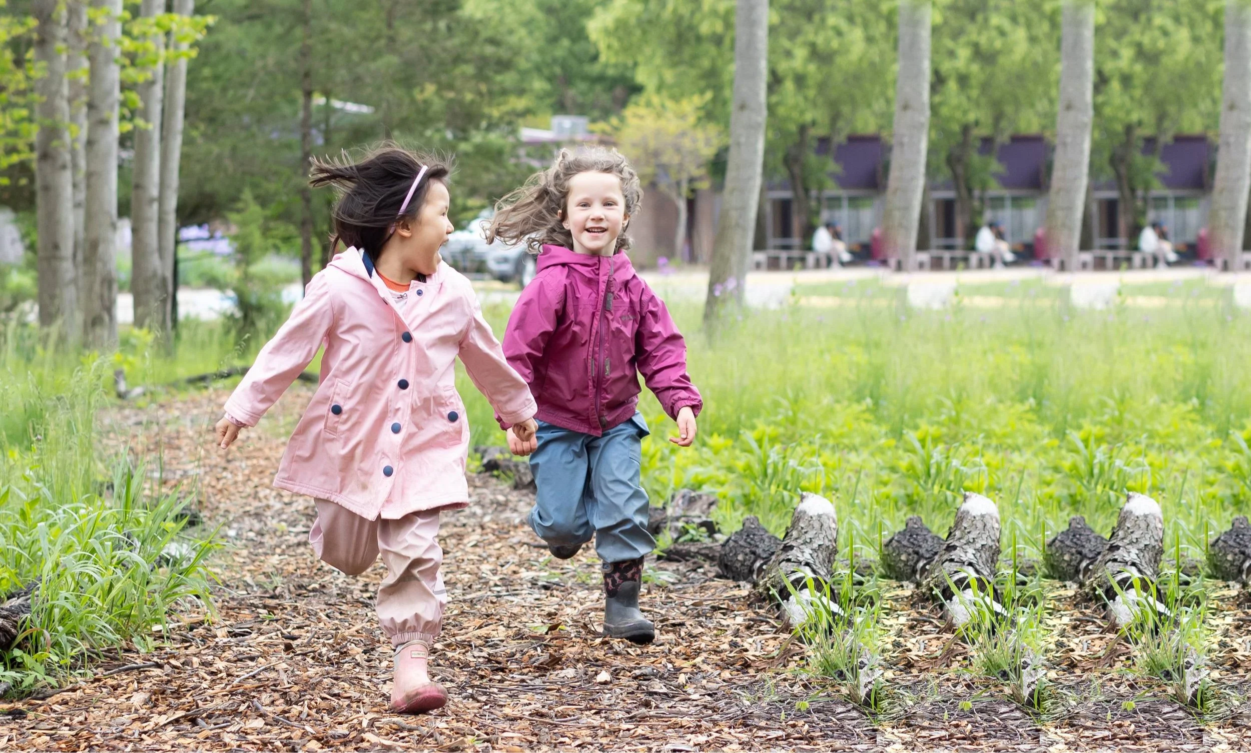 Two girls in kindergarten at Rudolf Steiner School of Ann Arbor are running together down a path outside and smiling.
