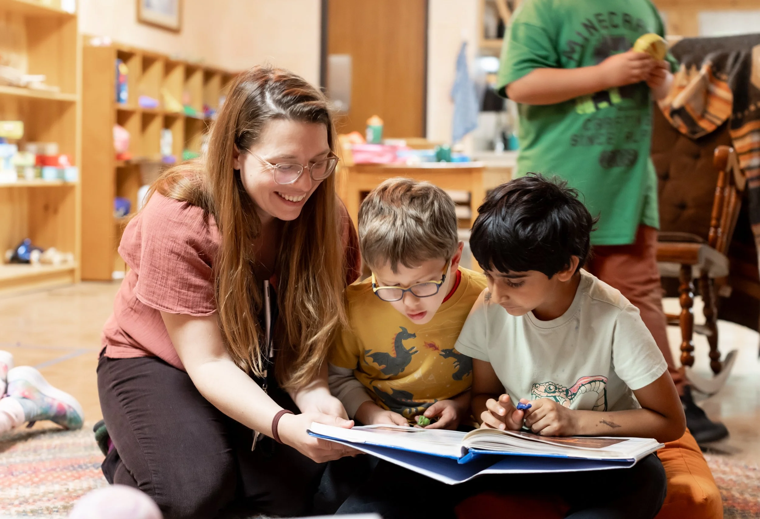 A smiling teacher is reading with two young students in the elementary school at the Rudolf Steiner School of Ann Arbor.