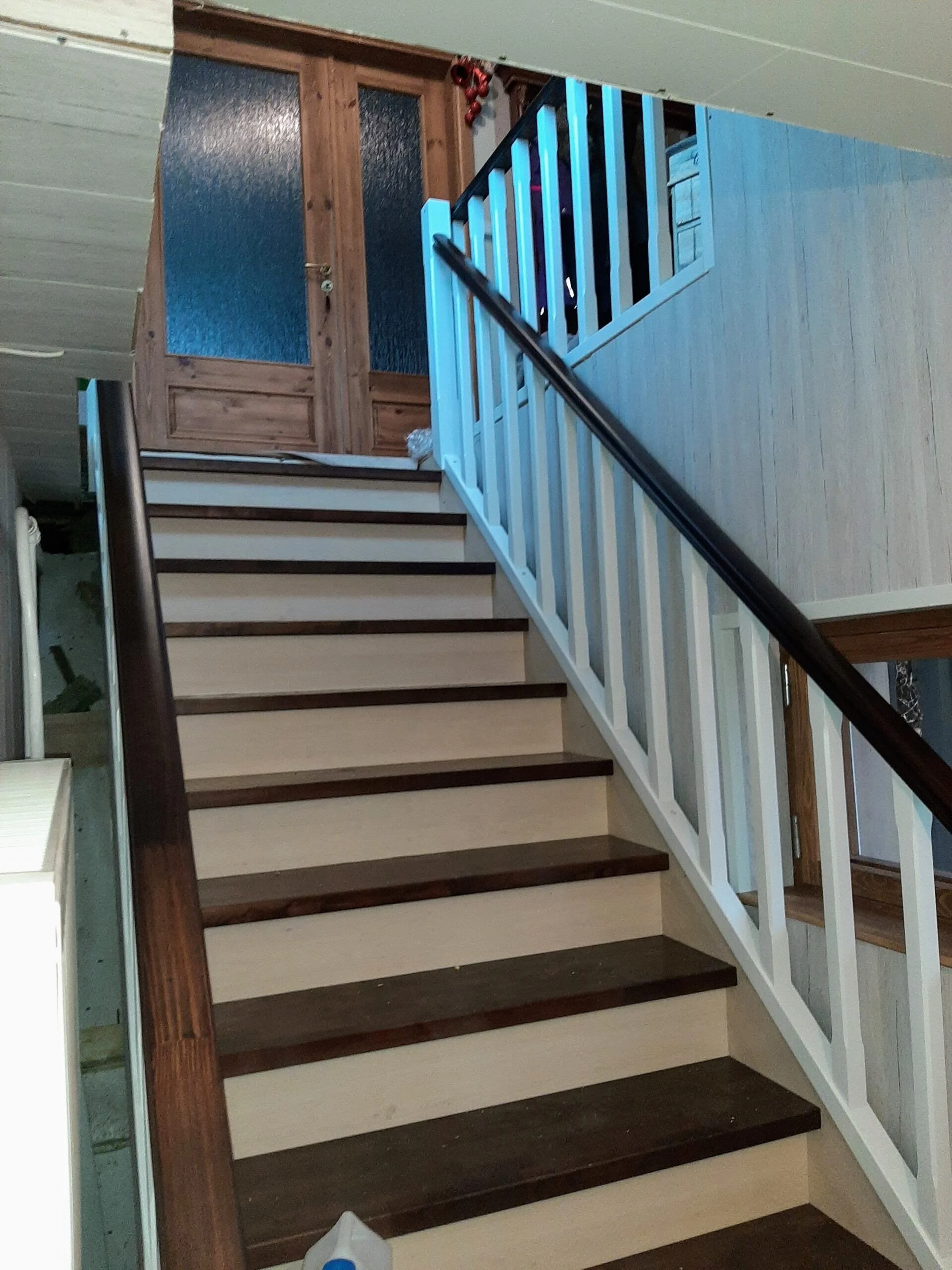 Interior view of a staircase with dark wood steps, a white painted railing, leading up to a wooden door with frosted glass panels.