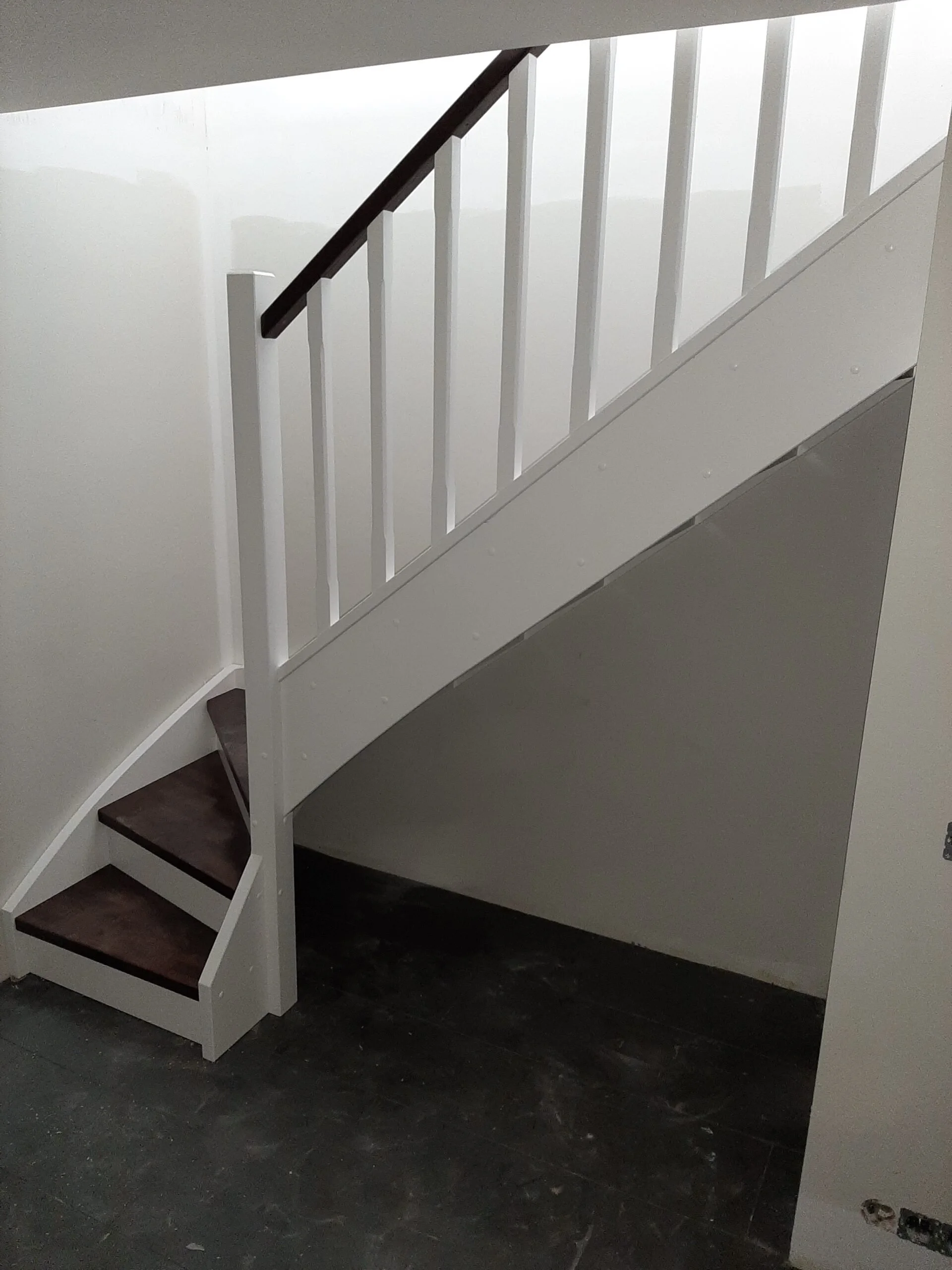 Photo of a staircase with dark wooden steps and a white railing, viewed from the bottom looking up.