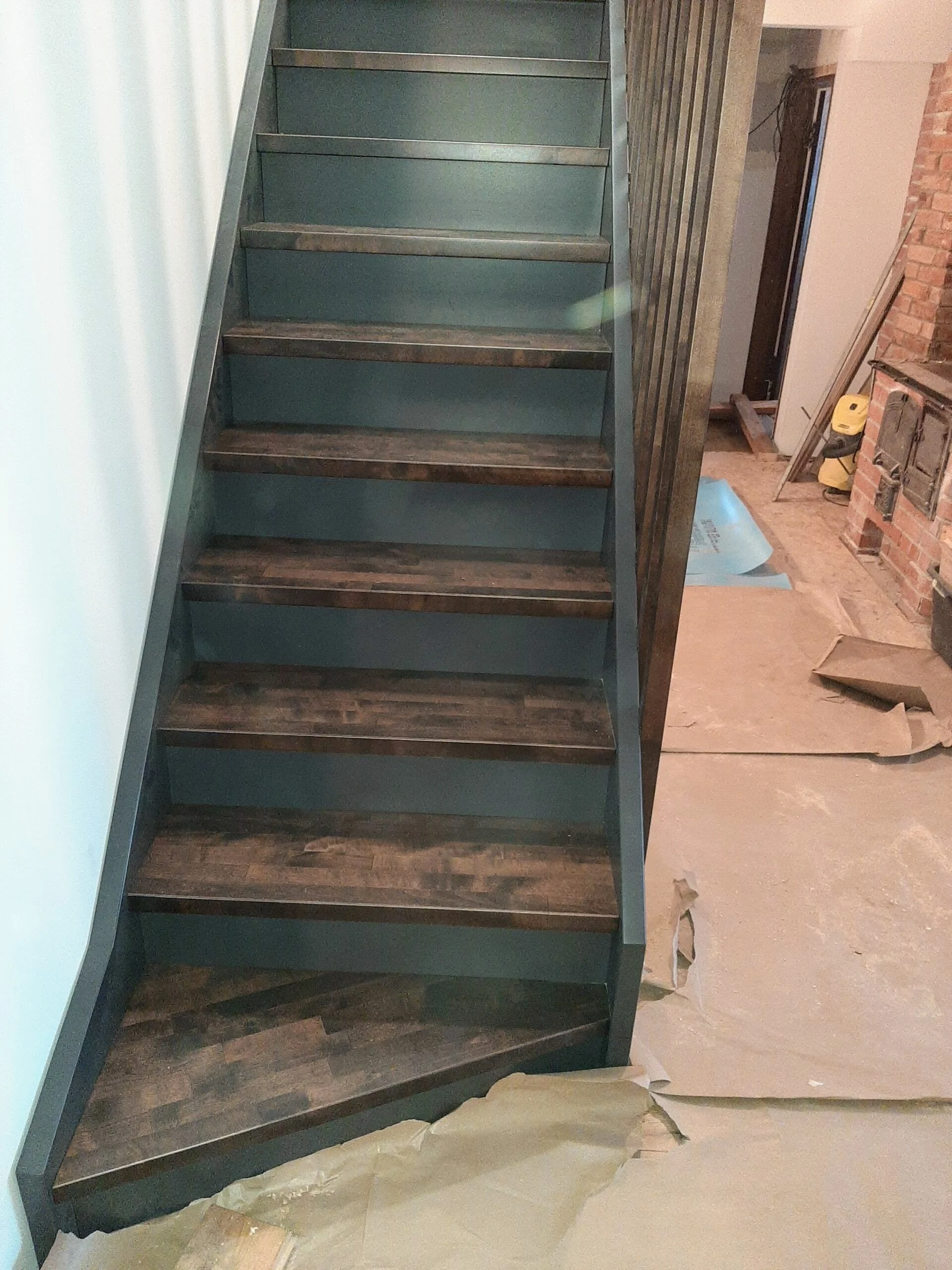 Interior view of a staircase with dark wooden steps and black risers, surrounded by construction materials and partially finished drywall.