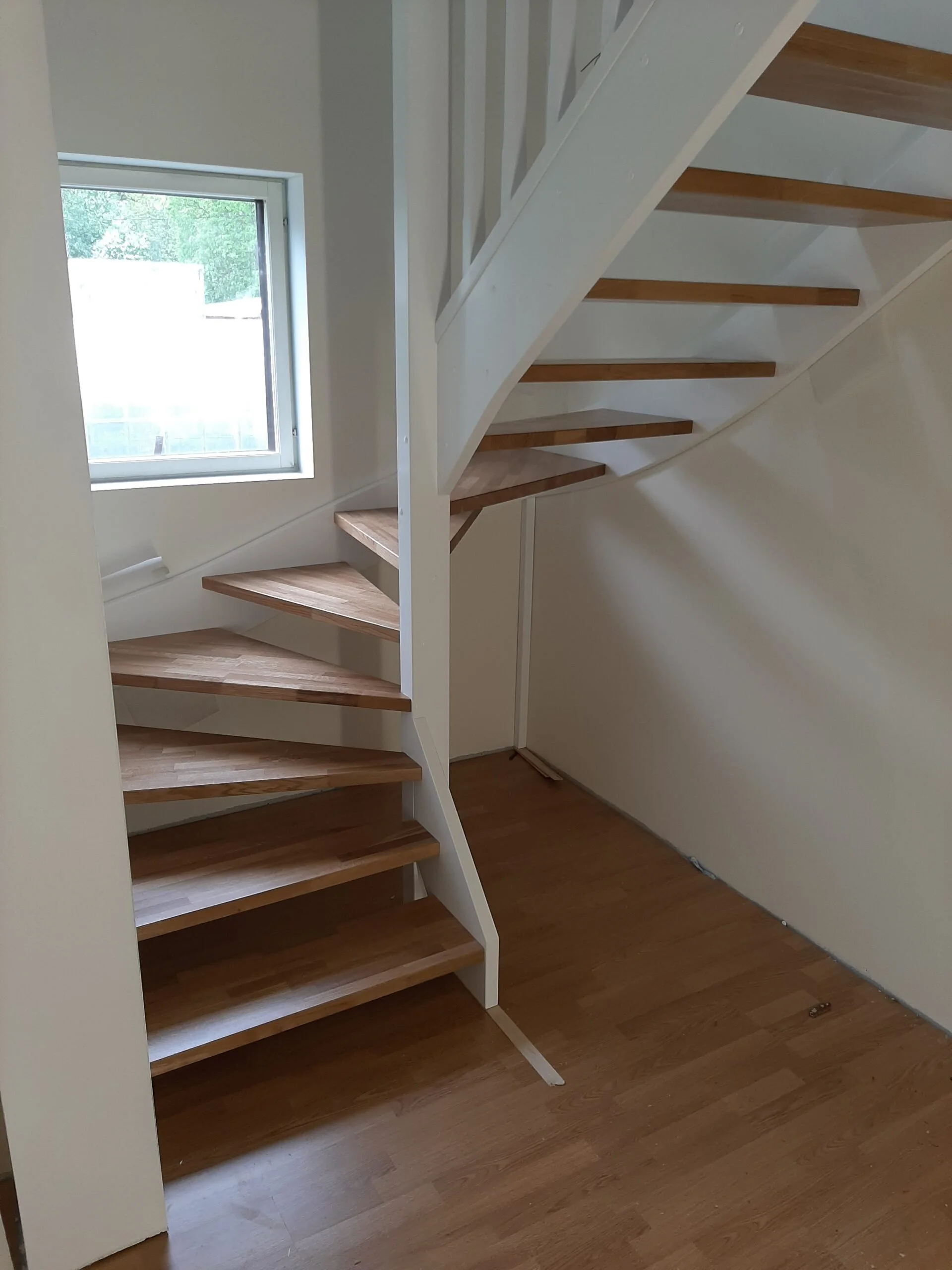 A wooden staircase with white railing inside a room near a window.