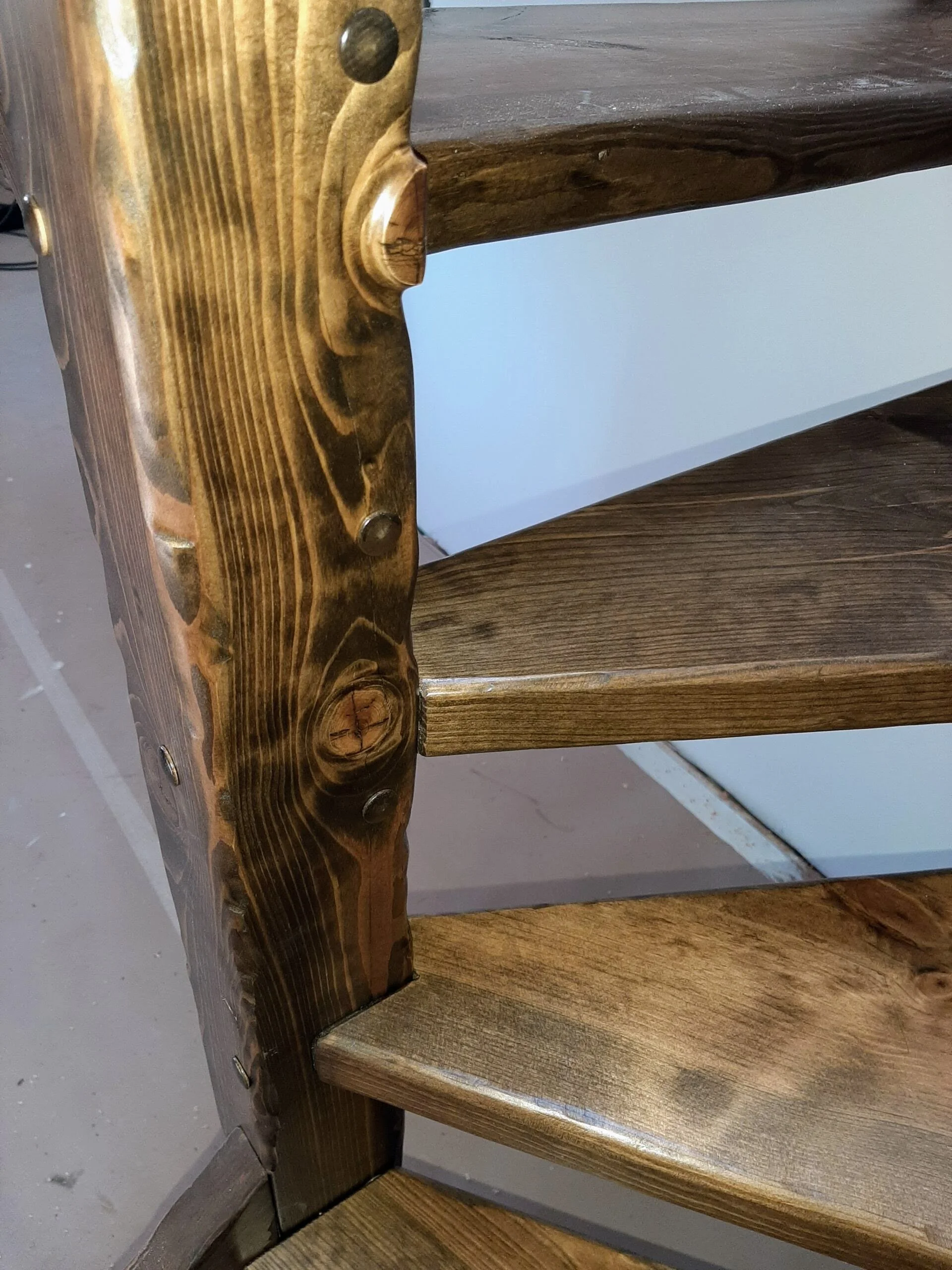 Close-up of a wooden staircase with visible nails, showing the natural wood grain and a white wall in the background.