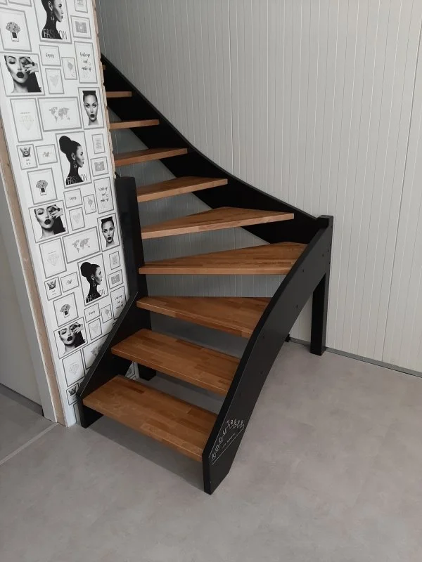 Indoor staircase with wooden steps and black sides next to a wall decorated with black-and-white framed photographs.