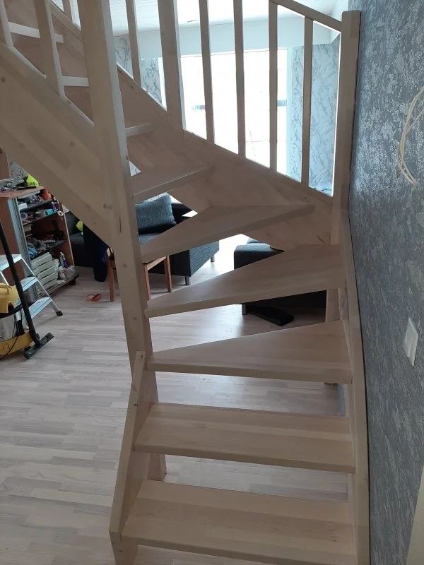 Wooden staircase inside a home, with a living room area and bookshelf visible in the background.