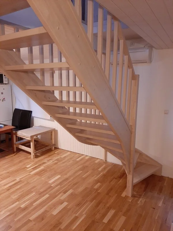 unfinished wooden staircase with railing inside a room with wood flooring and white walls.