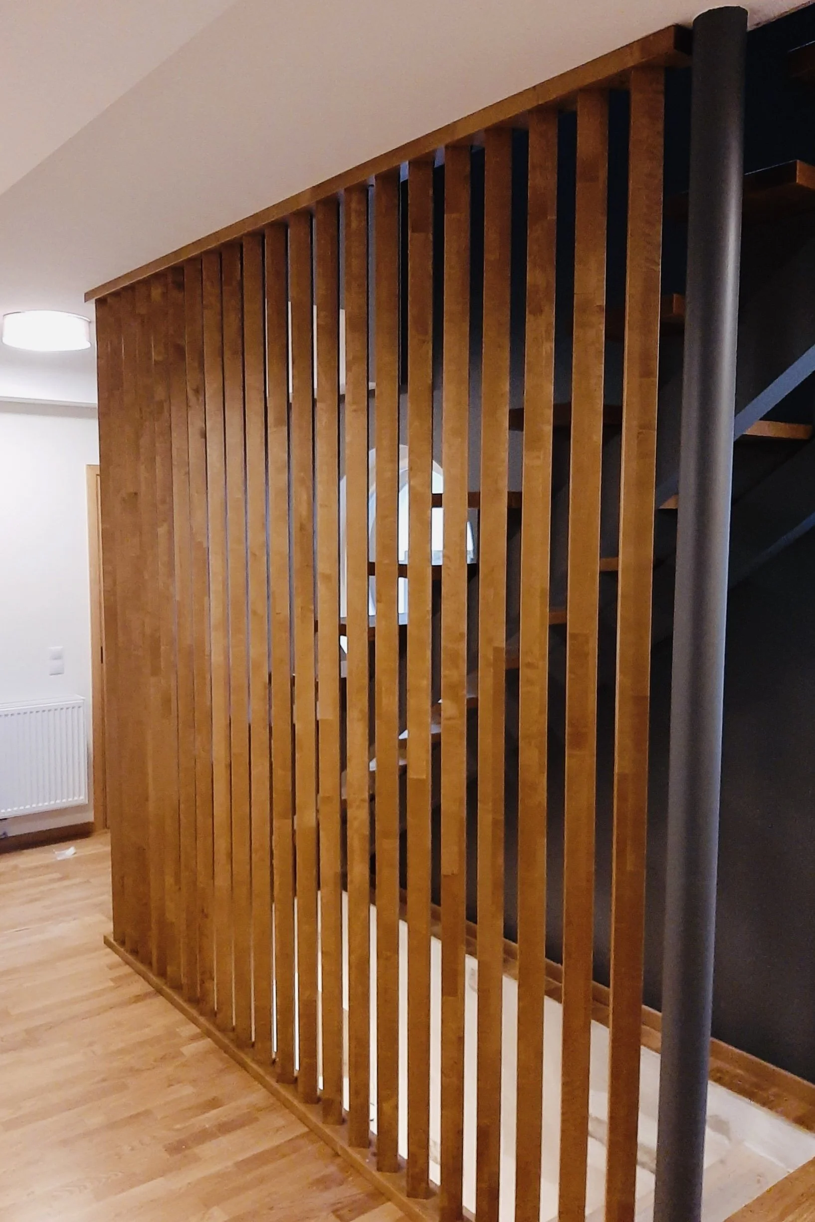 Wooden slatted room divider separating a staircase from the living space.