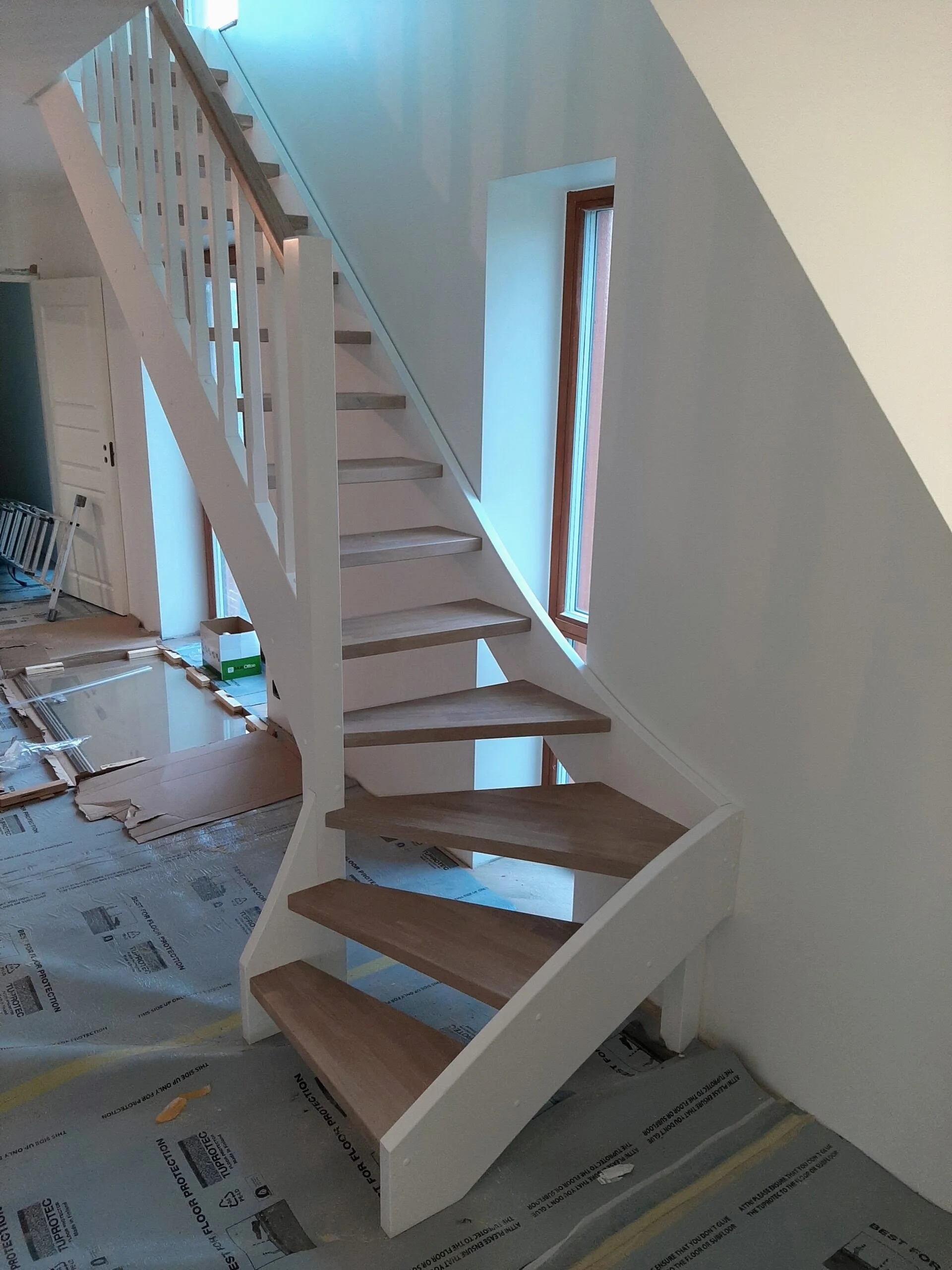 An interior staircase with unfinished wood steps and white trim, leading to a second level, with windows on the wall next to the stairs, during construction.