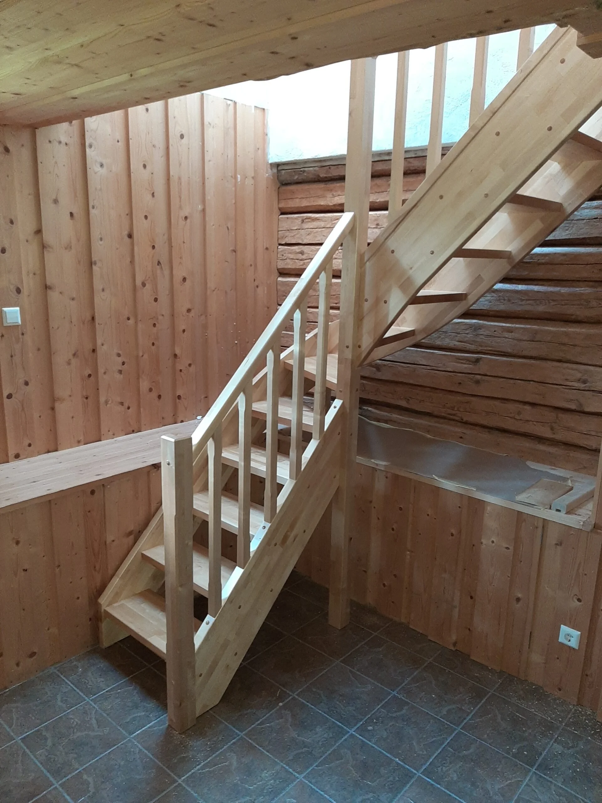 Wooden staircase under construction inside a room with wood-paneled walls and tile flooring.