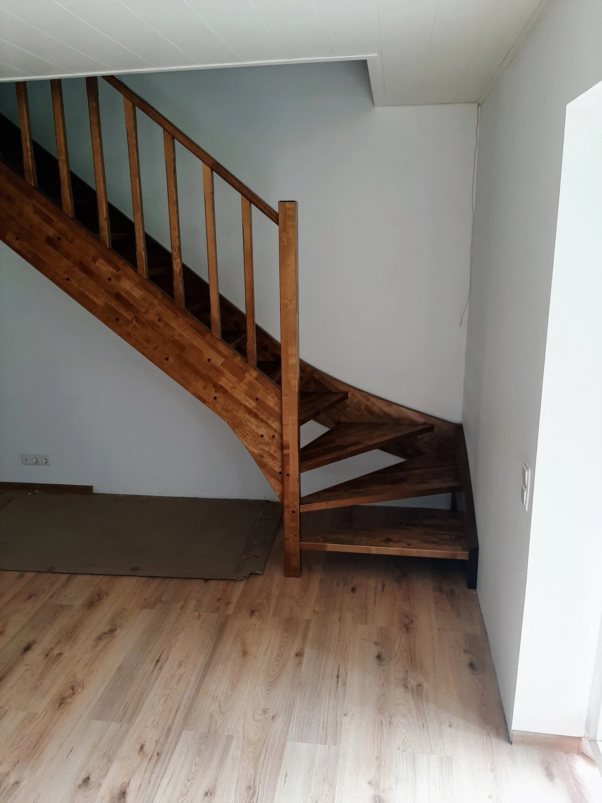 Wooden staircase inside a house with light-colored walls and wooden flooring.