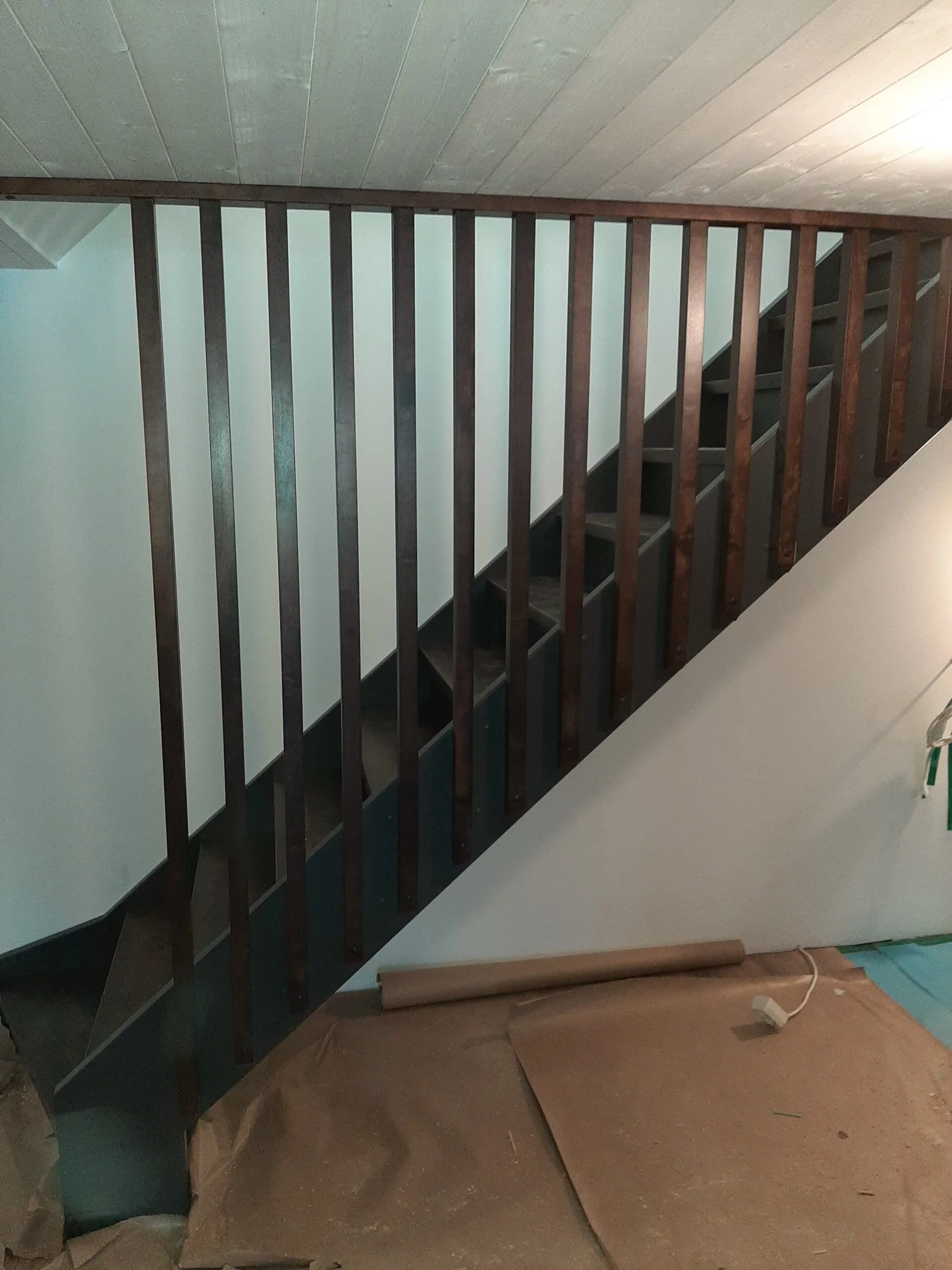 A staircase with wooden railing in an indoor setting under construction or renovation, with construction materials and paper on the floor.