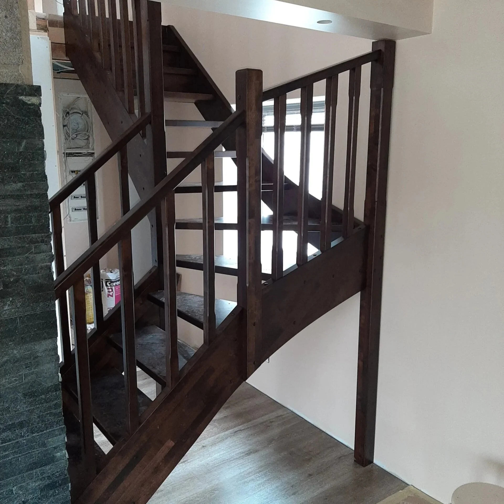 A dark wooden staircase with a railing leading to an upper level, situated next to a beige wall and a green wall section to the left.