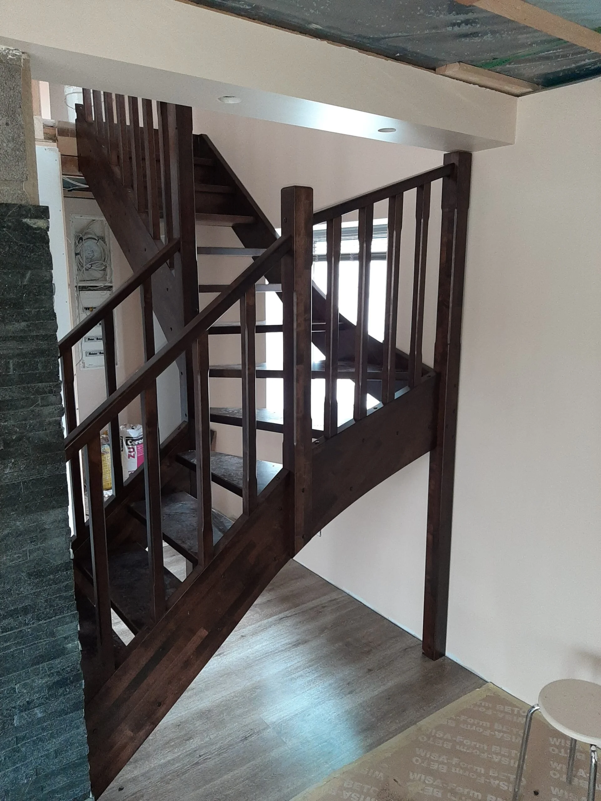 Interior view of a staircase with dark wood railings and steps, leading to an upper floor, near a large window letting in natural light.