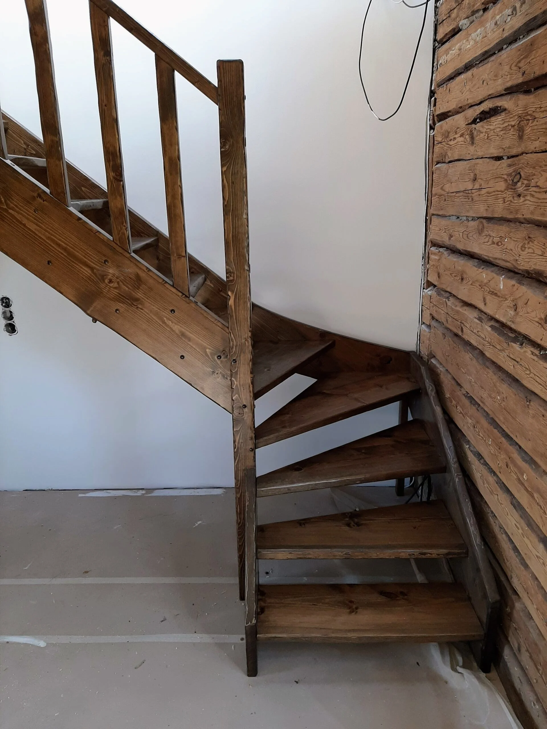 Interior view of wooden staircase with unfinished walls, showing stairs and railing, and exposed electrical wiring.