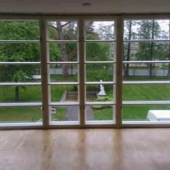 View through a large window showing a grassy yard with trees, a small statue, and a white fence outside.