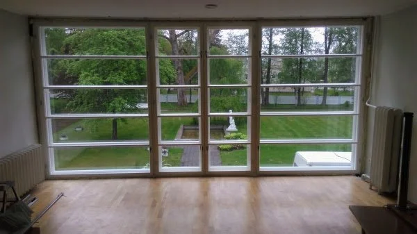 View of a backyard garden with a white statue and trees, seen through large glass windows in a room.