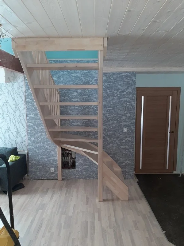 Wooden staircase with open risers leading to an upper level in a room with light wood flooring and a textured gray accent wall.