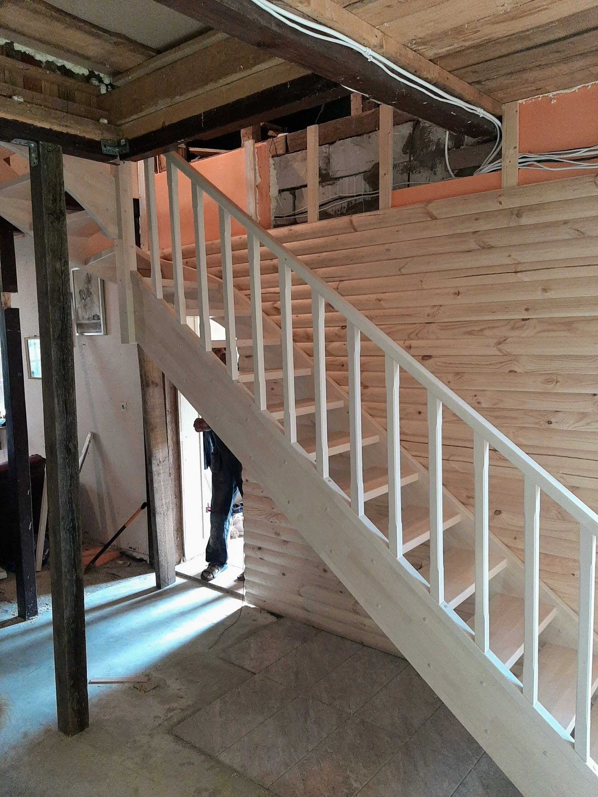 Construction of a wooden staircase in an unfinished room with exposed studs and electrical wiring.