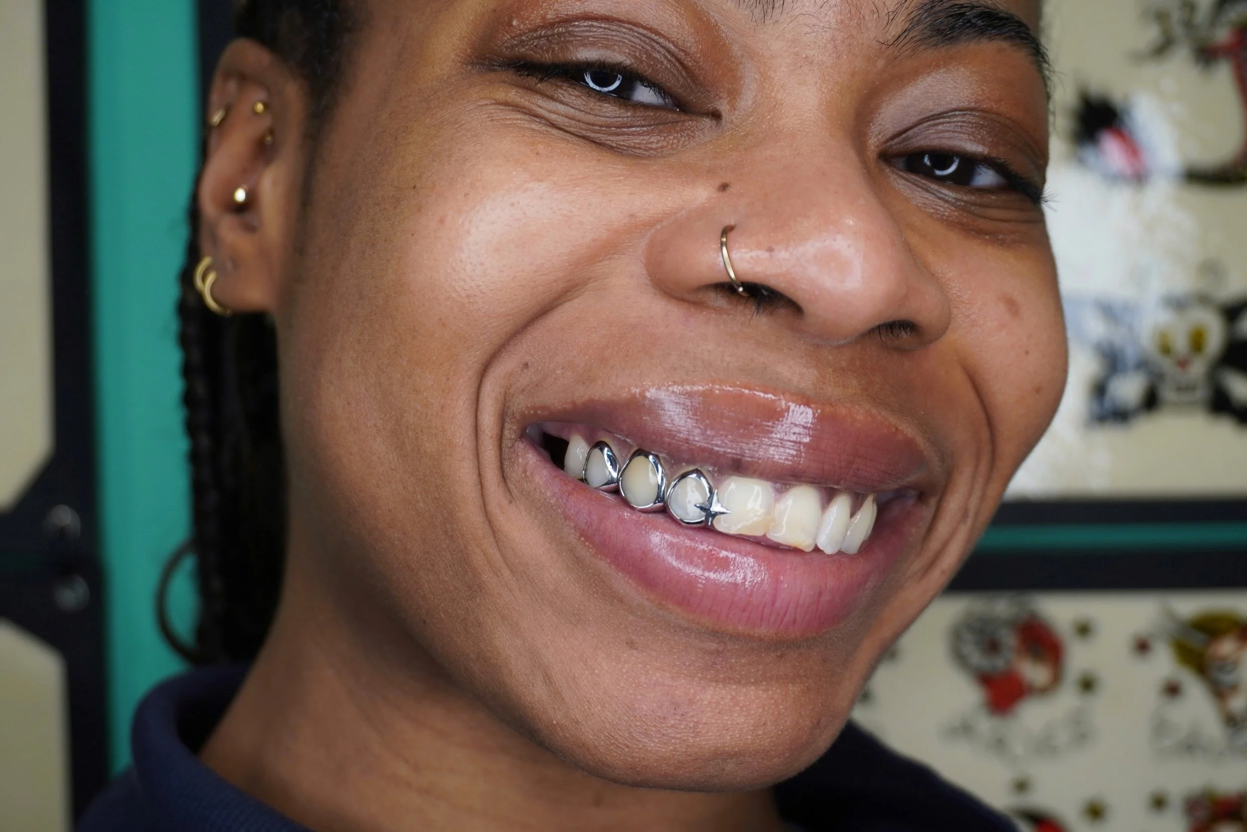 A smiling woman with multiple facial piercings, including a nose ring, and metal braces on her teeth.