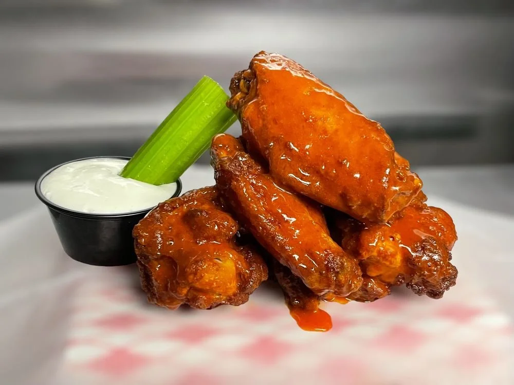Stack of glazed chicken wings with celery stick and dipping sauce.