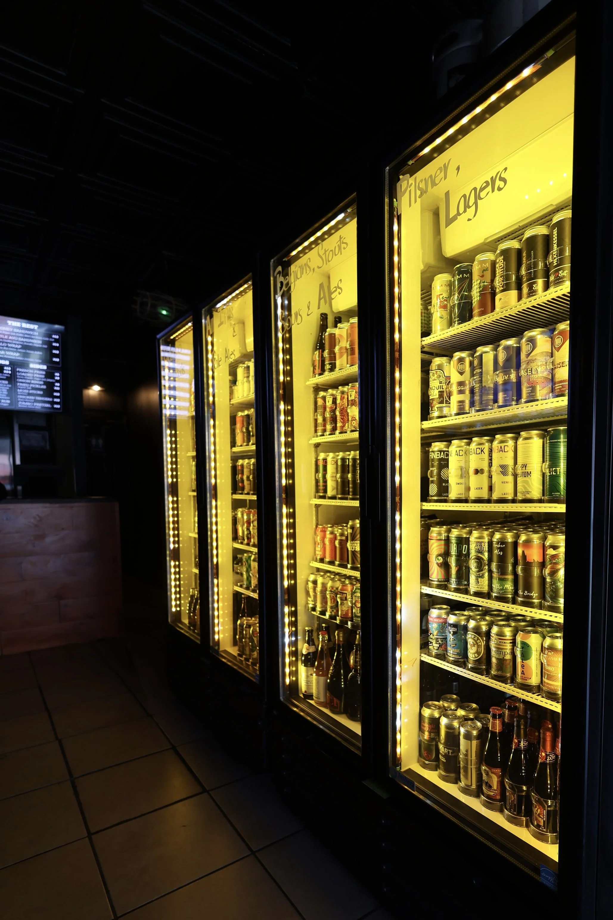 Vending machines with yellow lighting, stocked with various cans of beer.