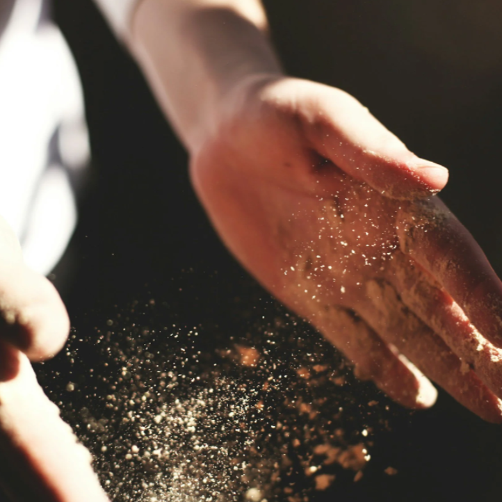 Close-up of a person's hand with flour sprinkled on fingers, falling onto a dark surface.