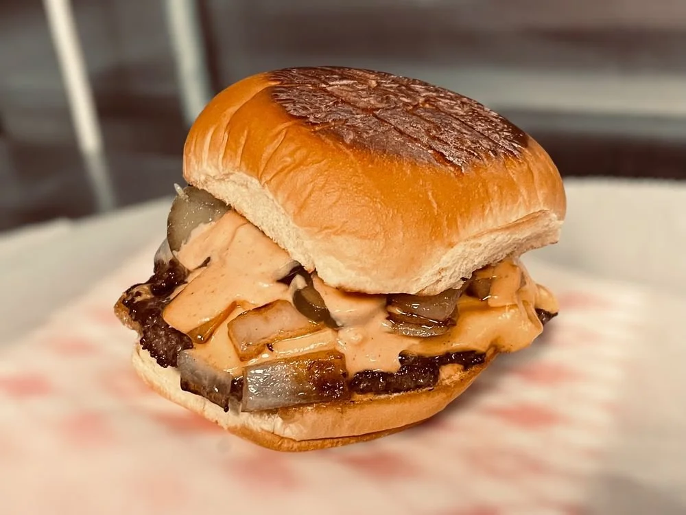 A burger with chopped onions and a creamy sauce in a toasted bun.